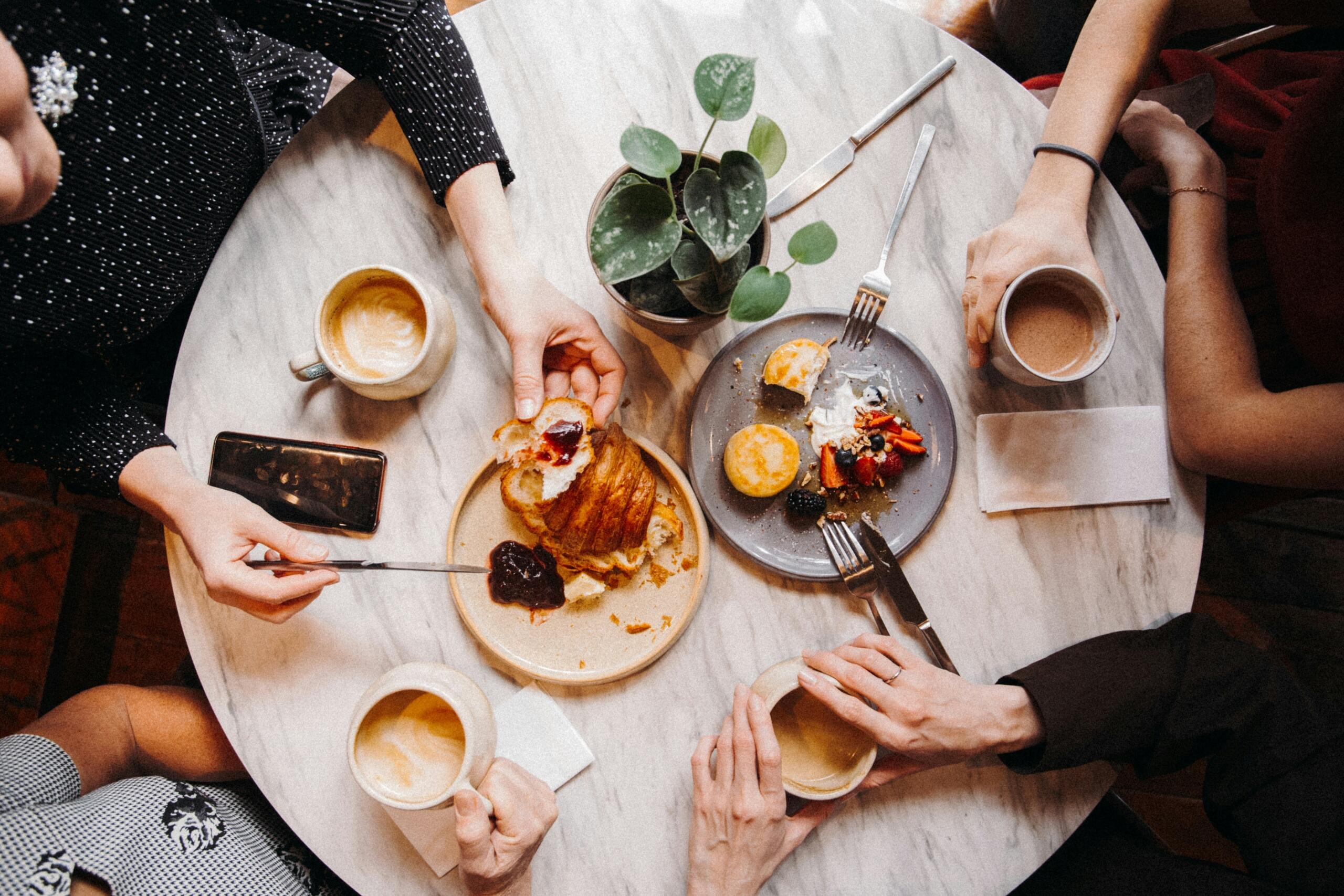 Several individuals seated at a table, sharing coffee and food in a friendly atmosphere.