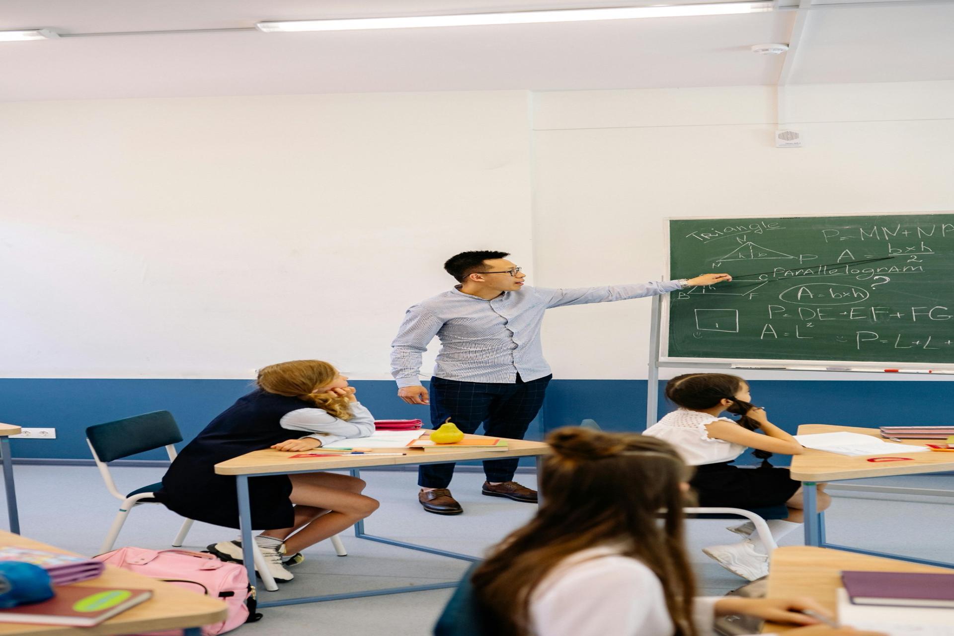 Students learning mathematics in a classroom with a teacher explaining geometry concepts on the board during an SPM maths lesson
