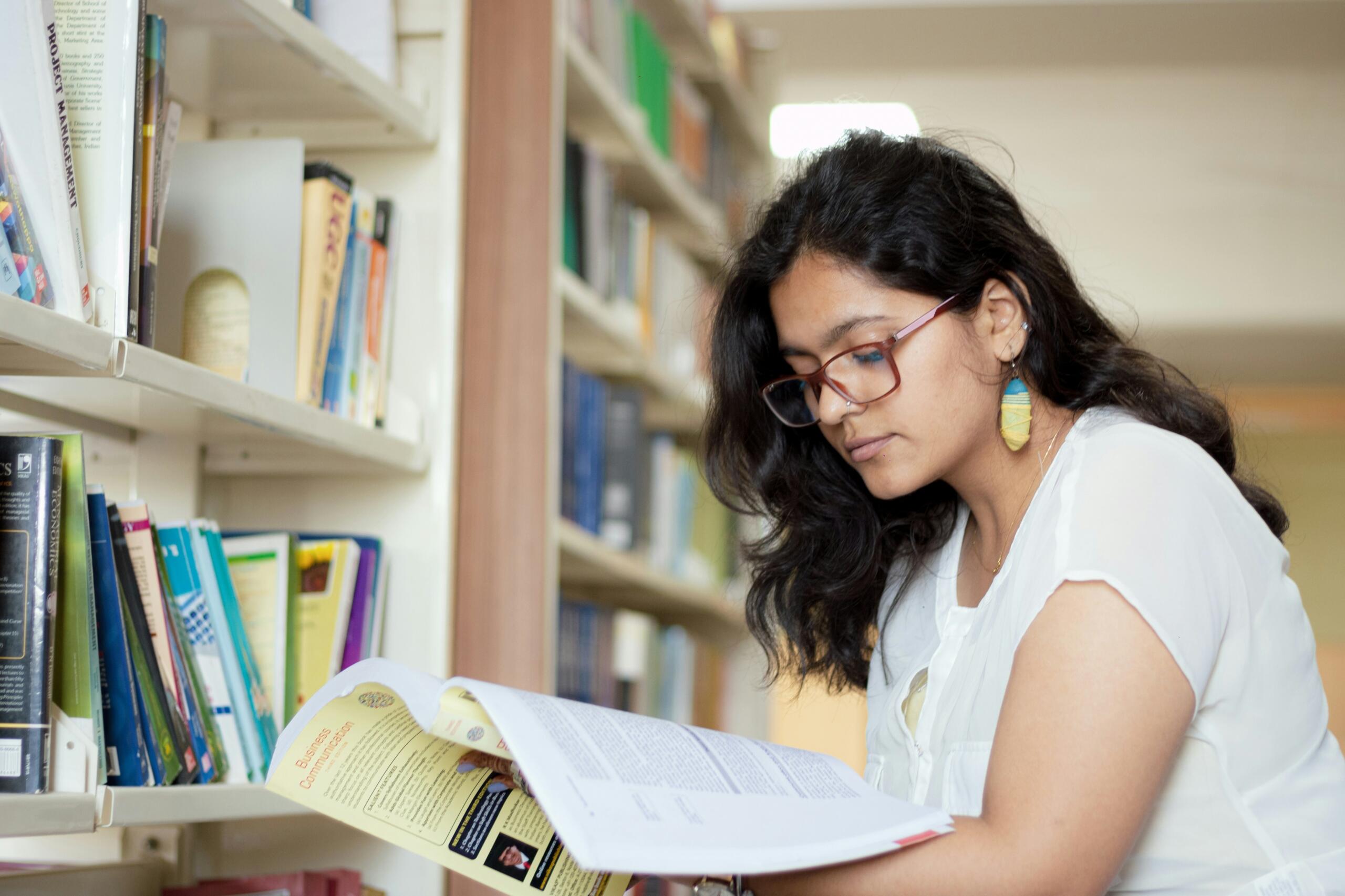 Portrait of a smiling young female student reading a book in a library.