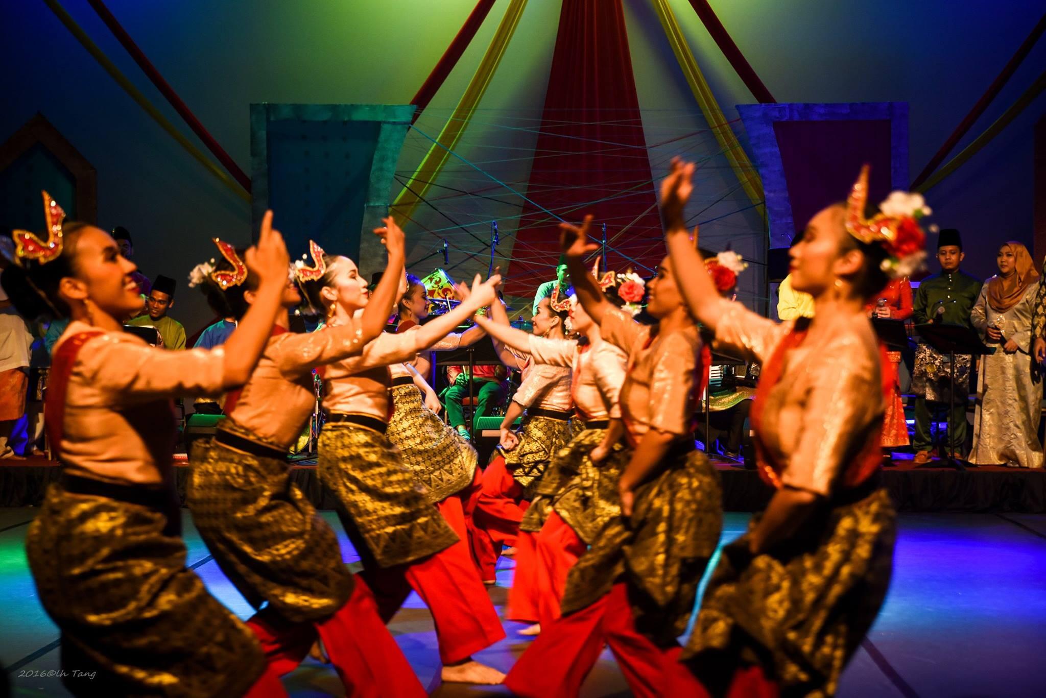 Colorful traditional dance performance with women in vibrant attire and ornate headpieces, gracefully moving in sync on stage under dramatic lighting.