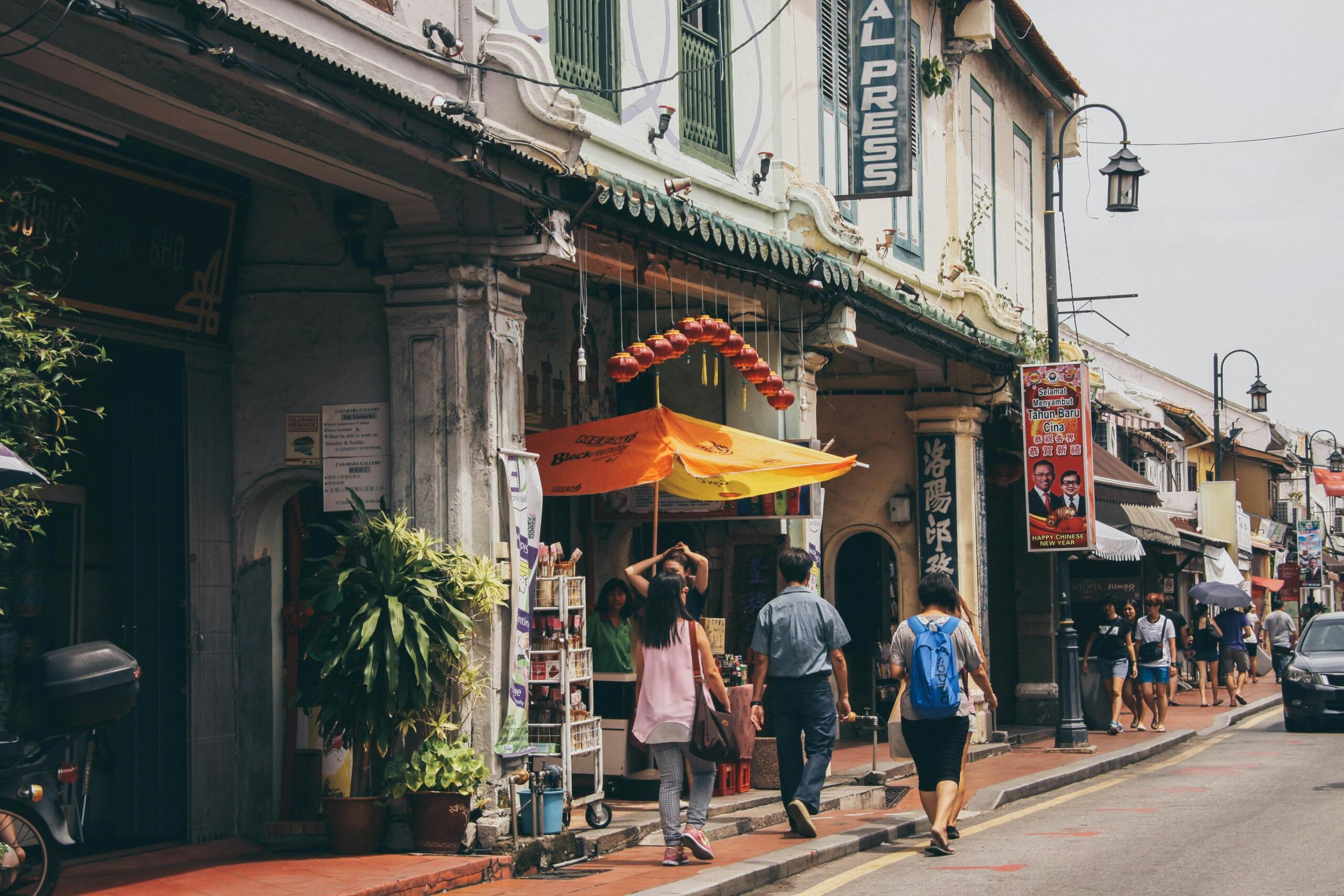 A busy street scene in Malaysia featuring pedestrians walking alongside a parked motorcycle.