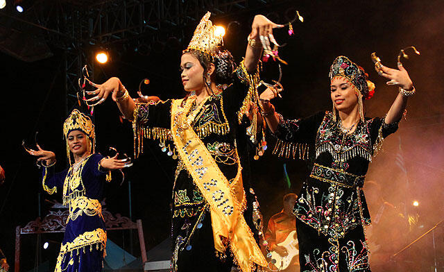 Igal igal dancers in ornate traditional costumes perform a cultural dance on stage, adorned with gold and colorful details, creating a joyful, festive atmosphere.
