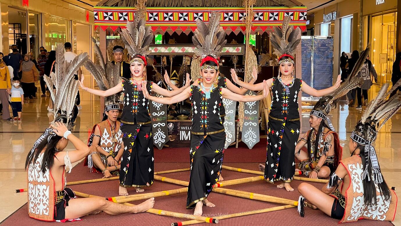 Traditional dance performance of Sabah in a mall, featuring dancers in elaborate feathered headdresses and black outfits, evoking cultural vibrancy and energy.