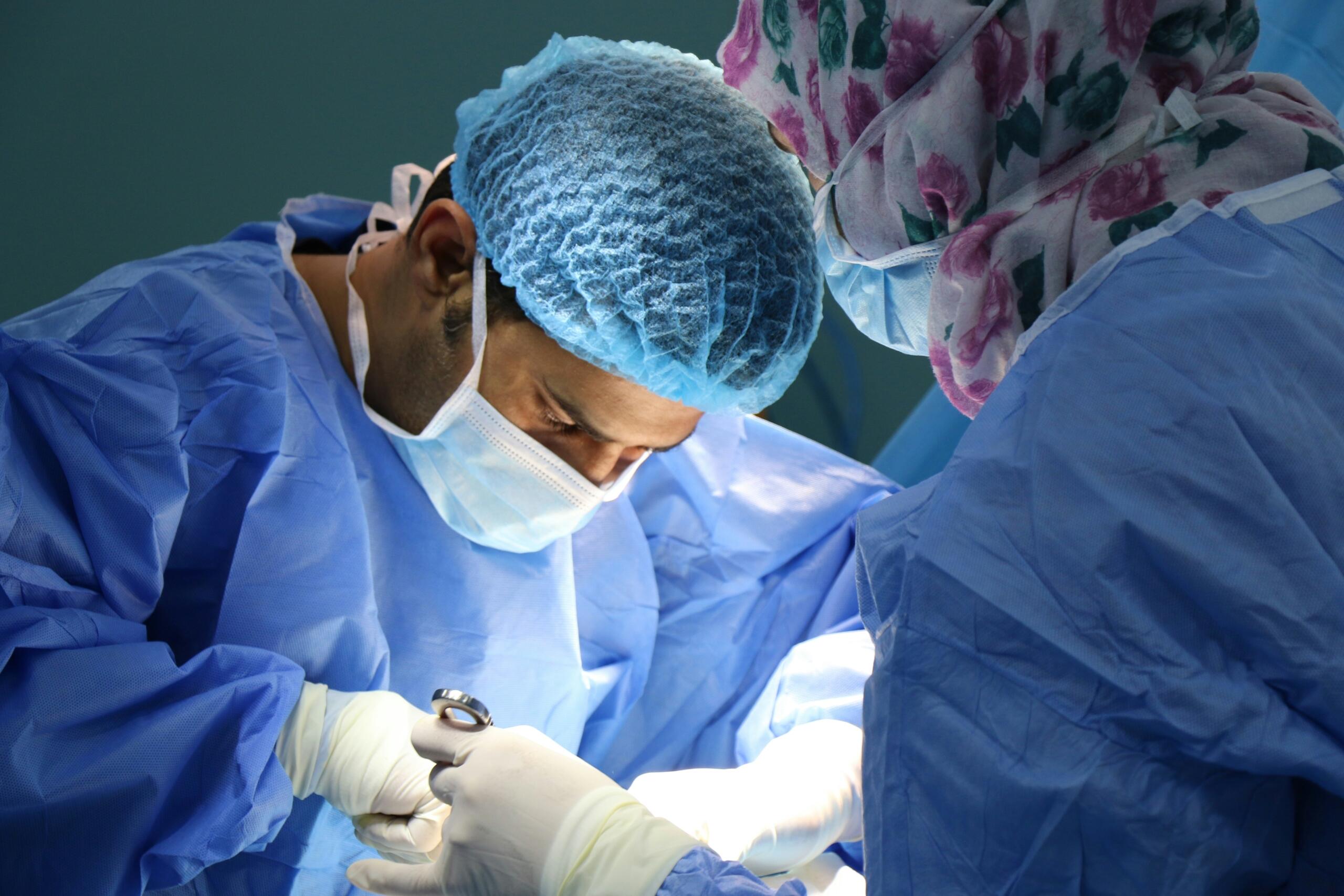 Two doctors dressed in medical gowns, performing an operation in an operating theatre.