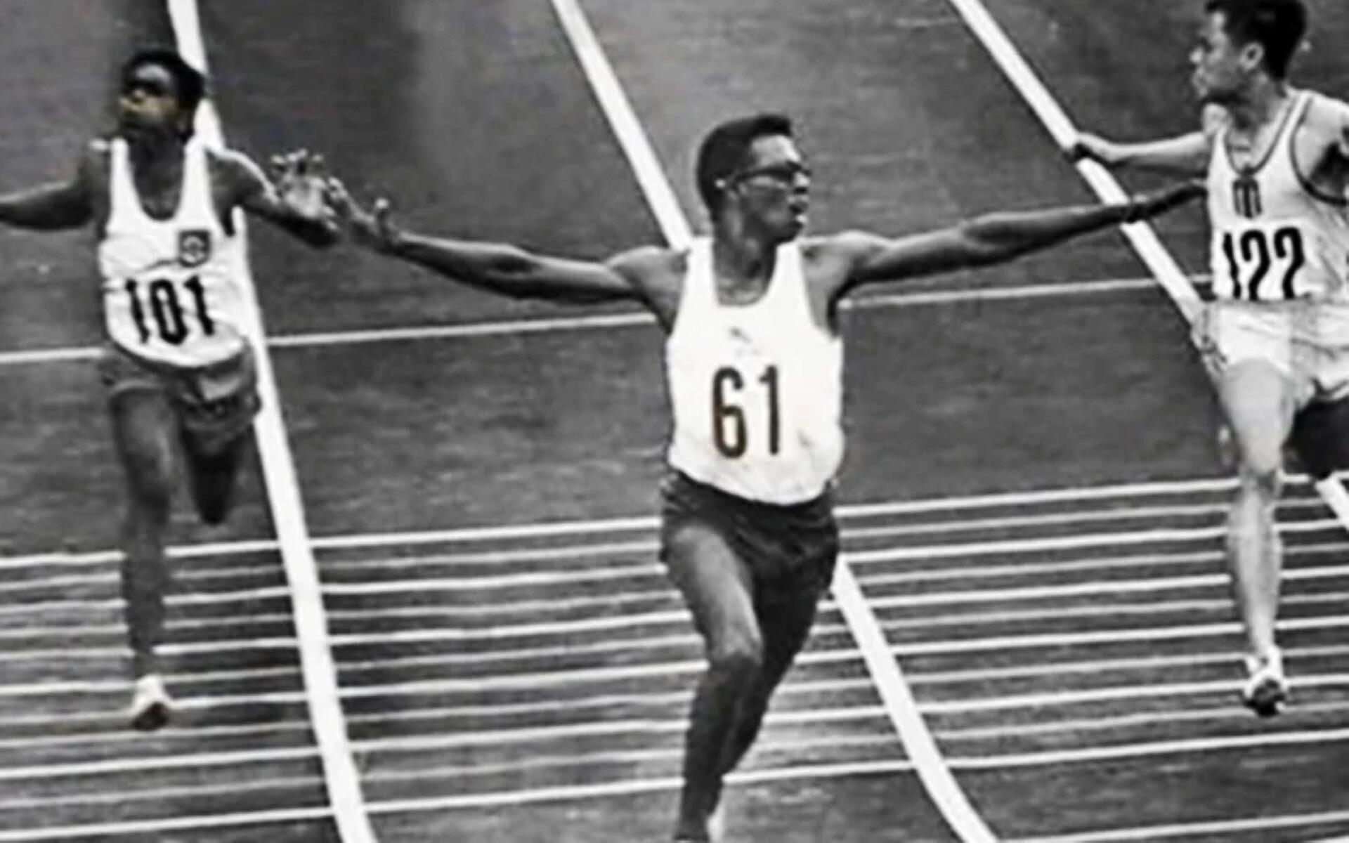 Black and white image of several men racing on a track, capturing the intensity of their competition.