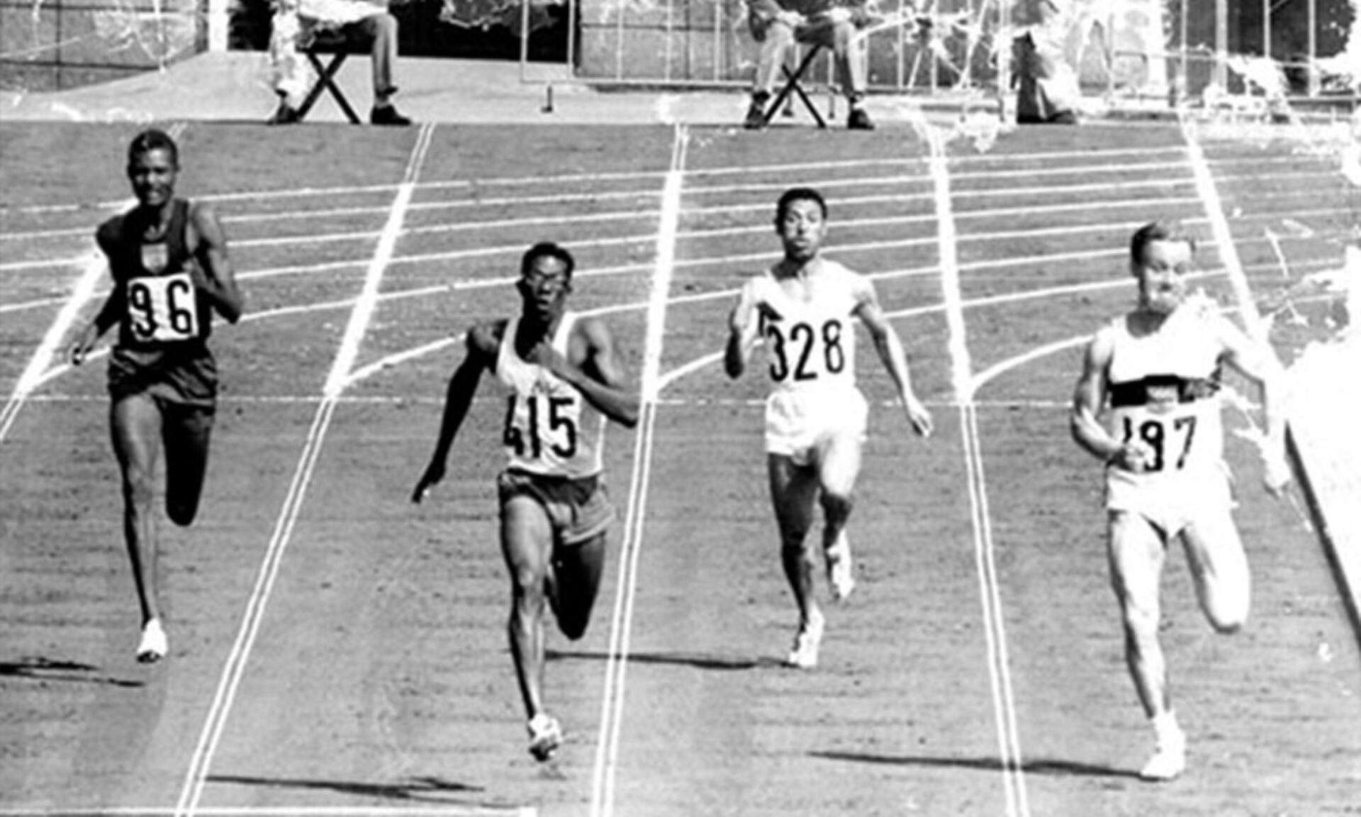 Black and white image of several men racing on a track, capturing the intensity of a running event.