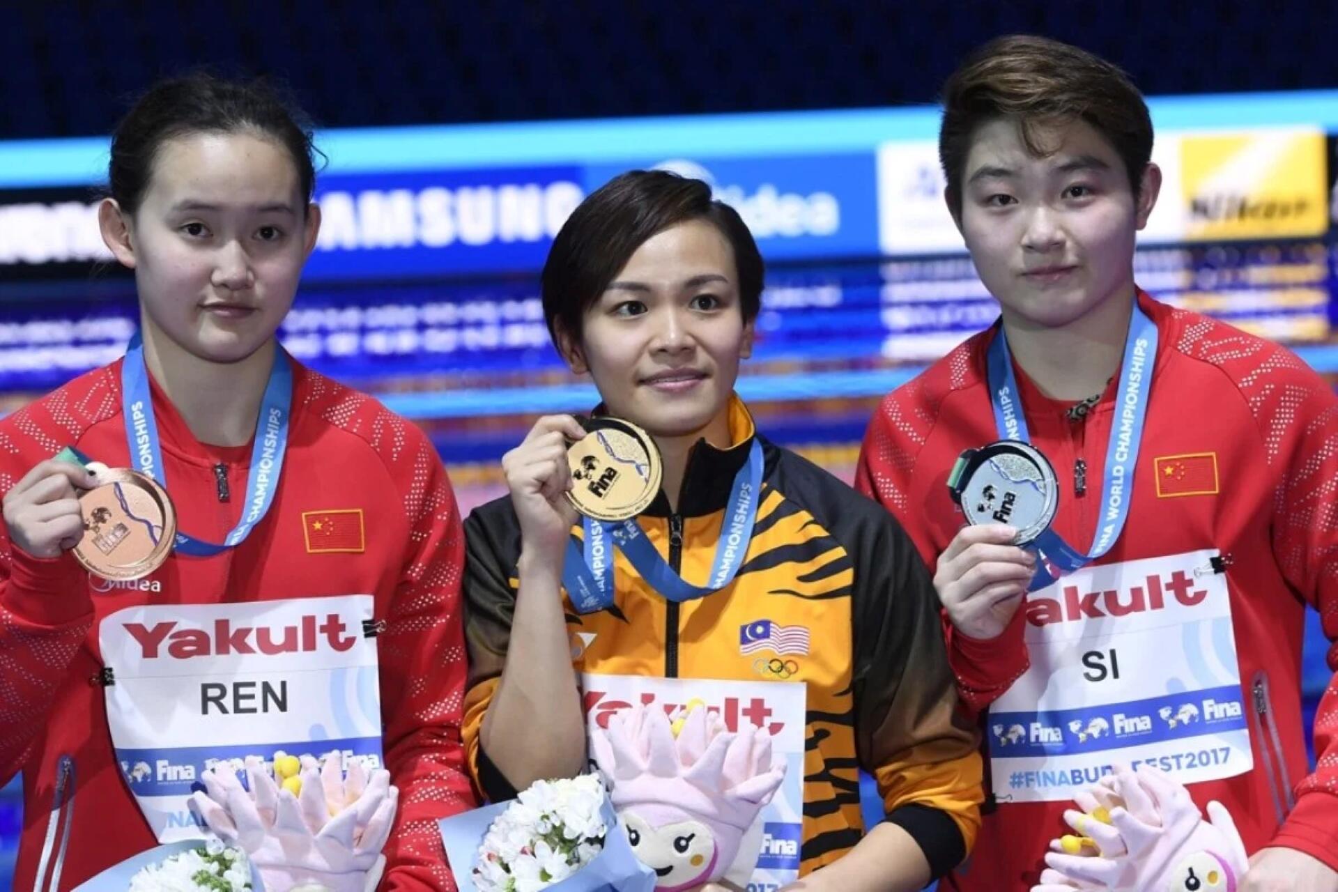 Three women proudly display their medals while posing together for the camera, smiling and celebrating their achievement.