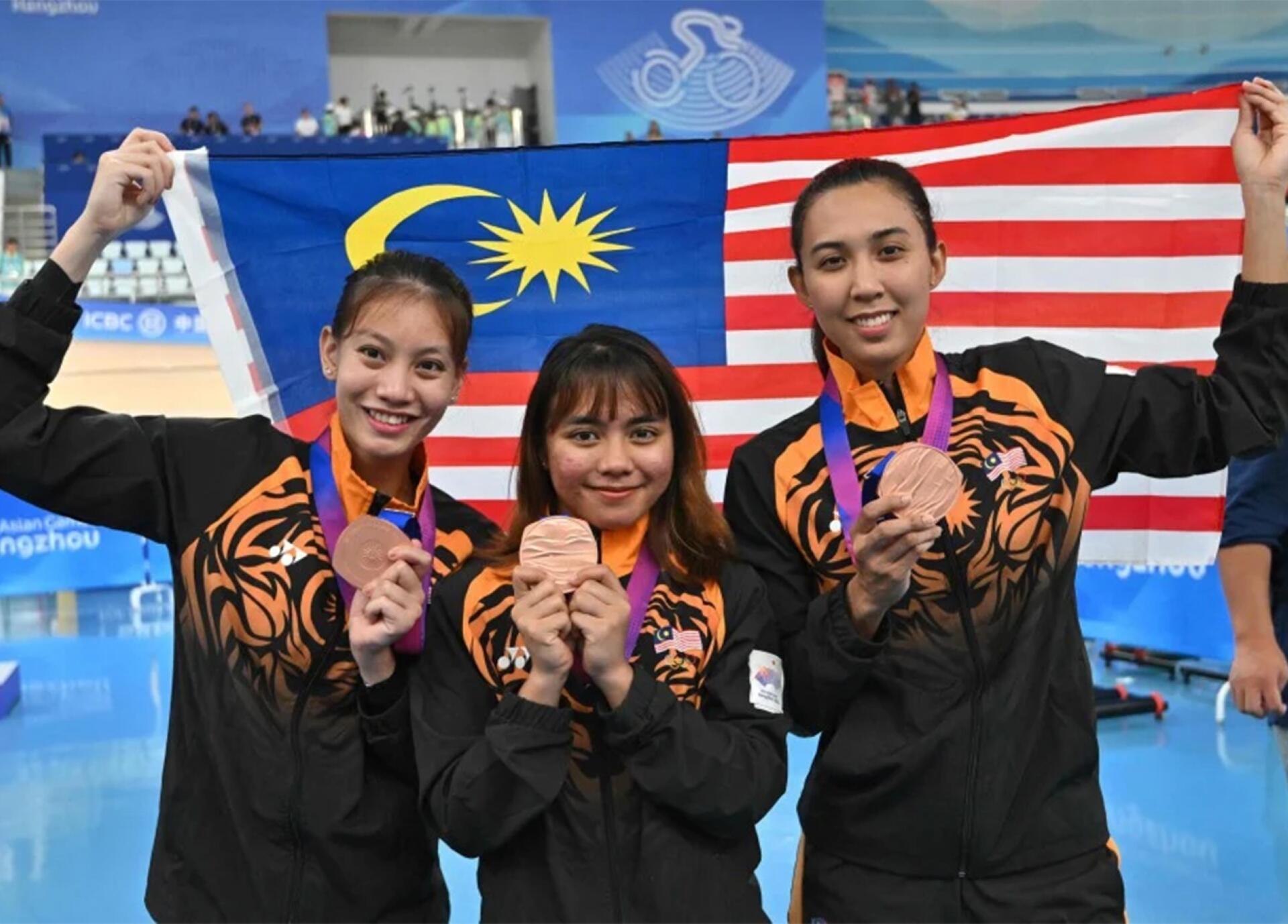 Malaysia's women's cycling team joyfully celebrates their gold medal victory, showcasing their pride and achievement.