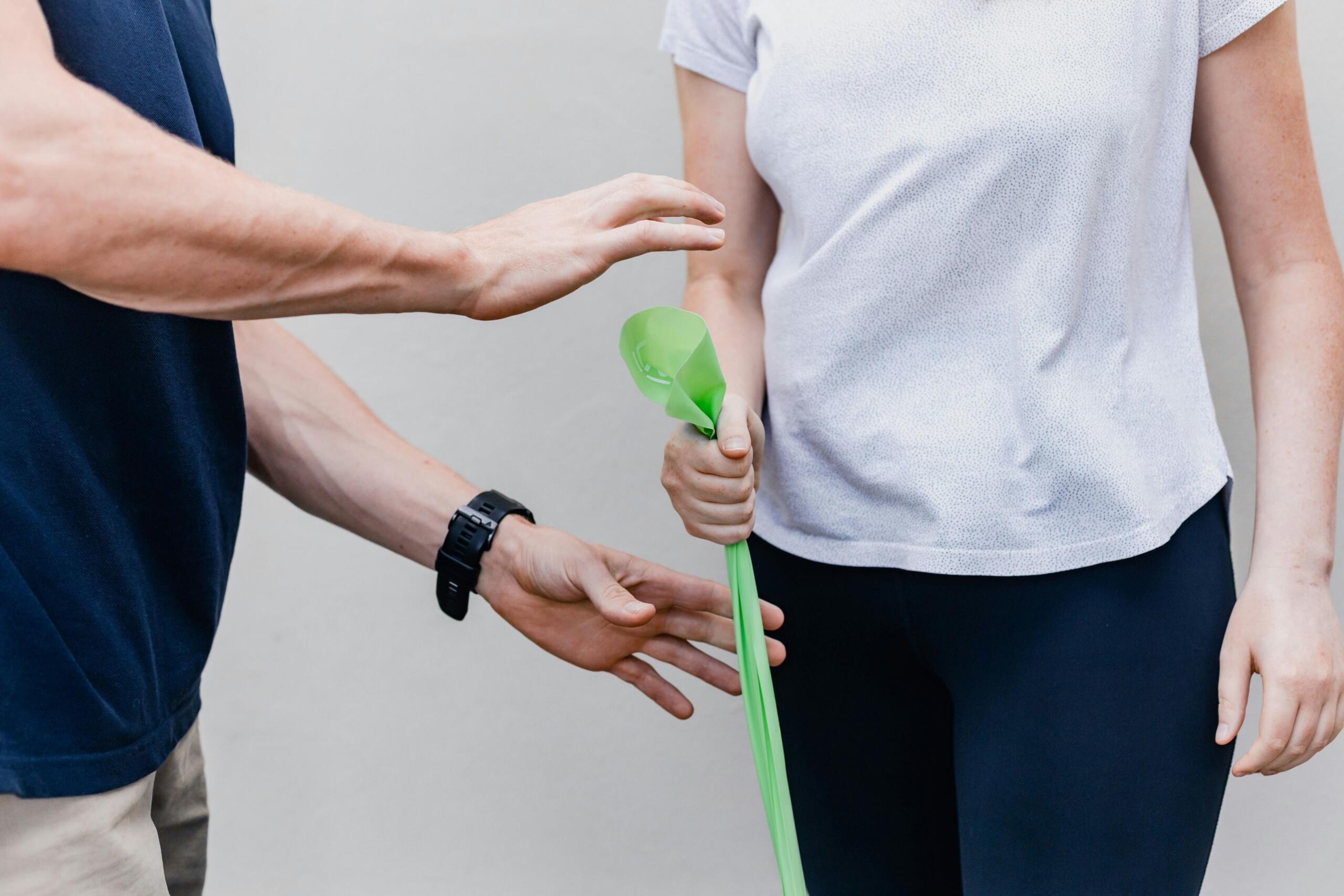 A person holding a green resistance band, guided by a physical therapist.