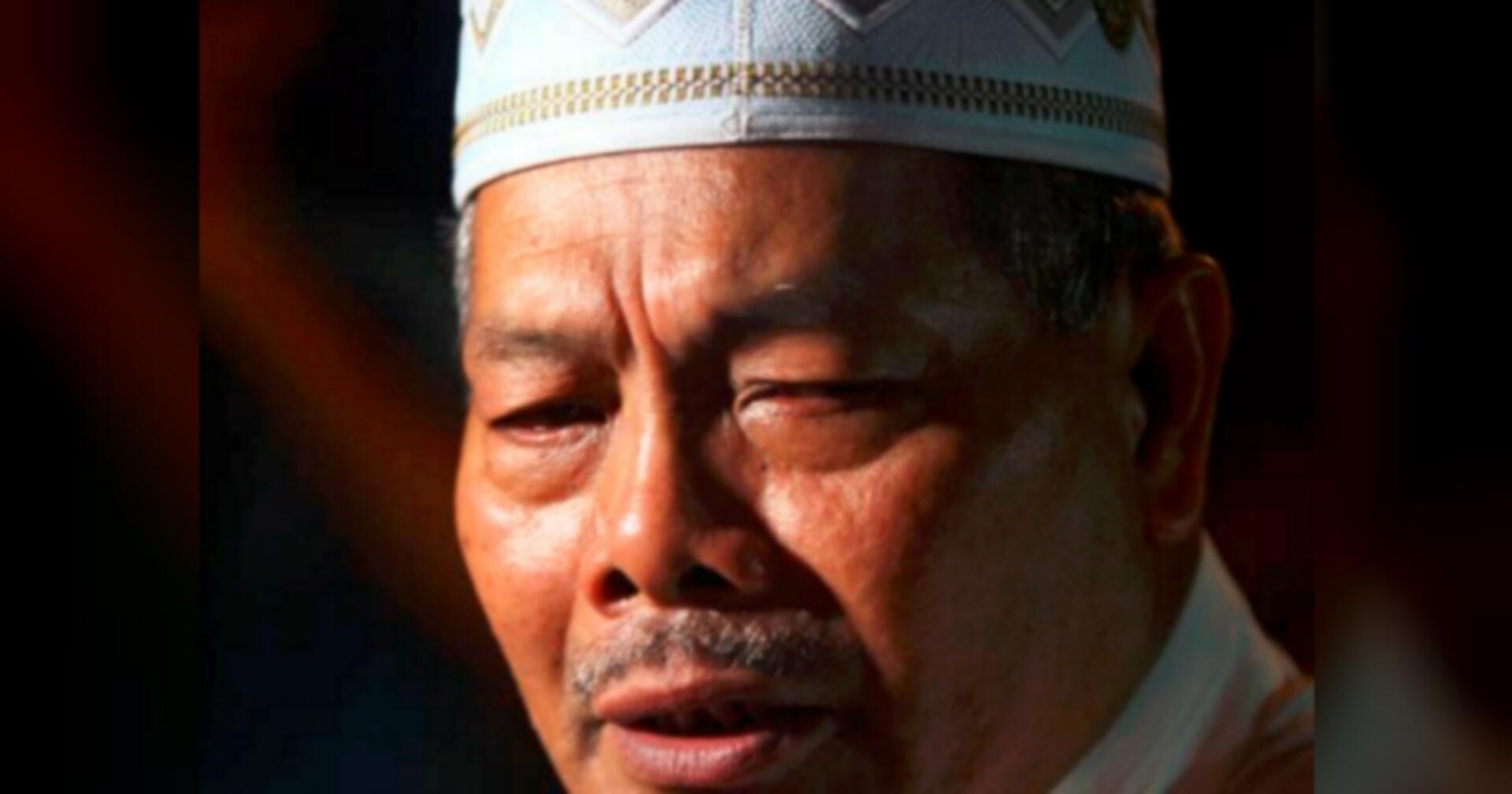 Elderly man wearing a white cap, expressing deep emotion or contemplation with closed eyes. The lighting is warm, highlighting his facial features.