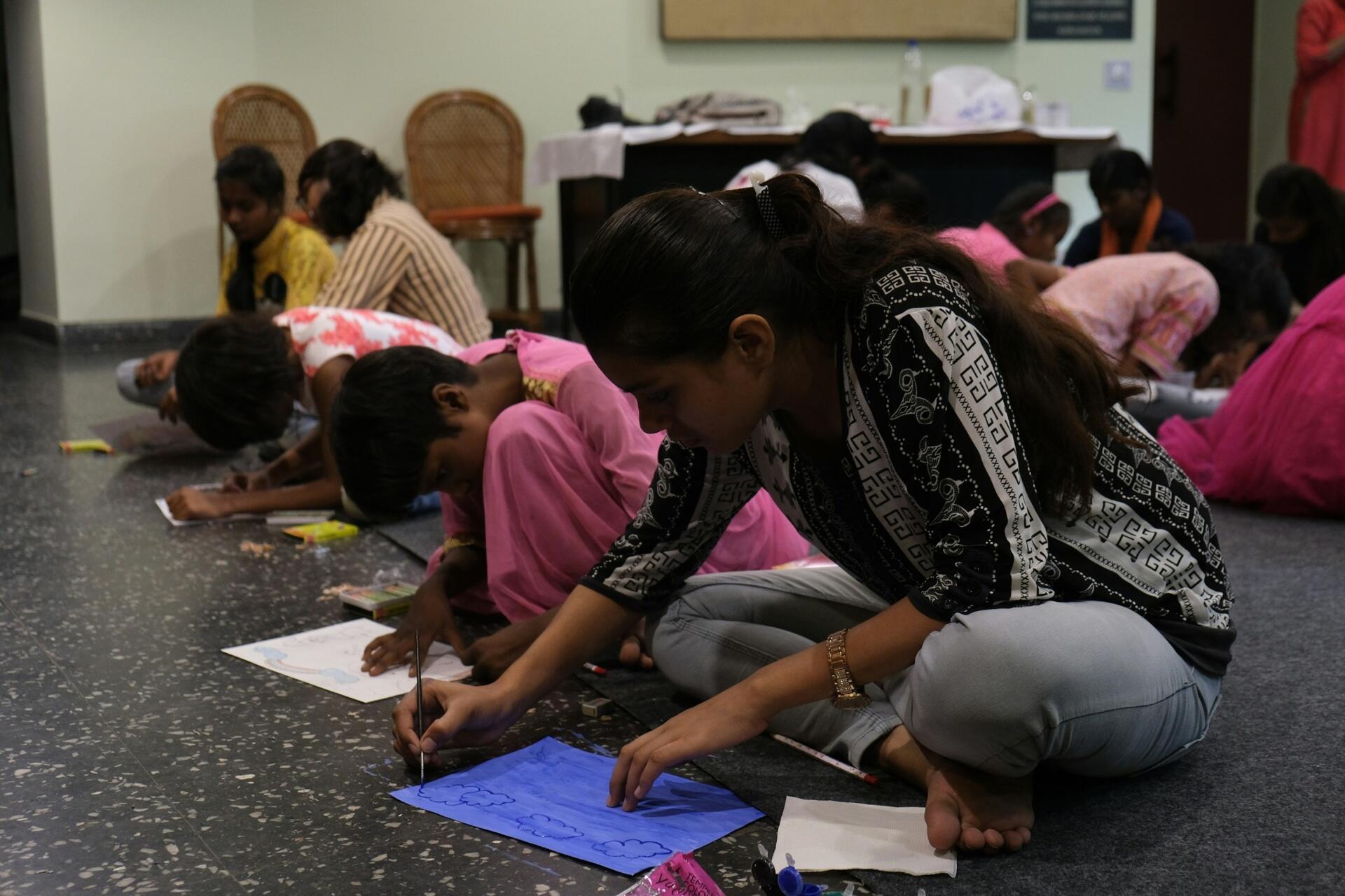 Children and young students sitting together indoors while drawing and participating in a community learning activity.