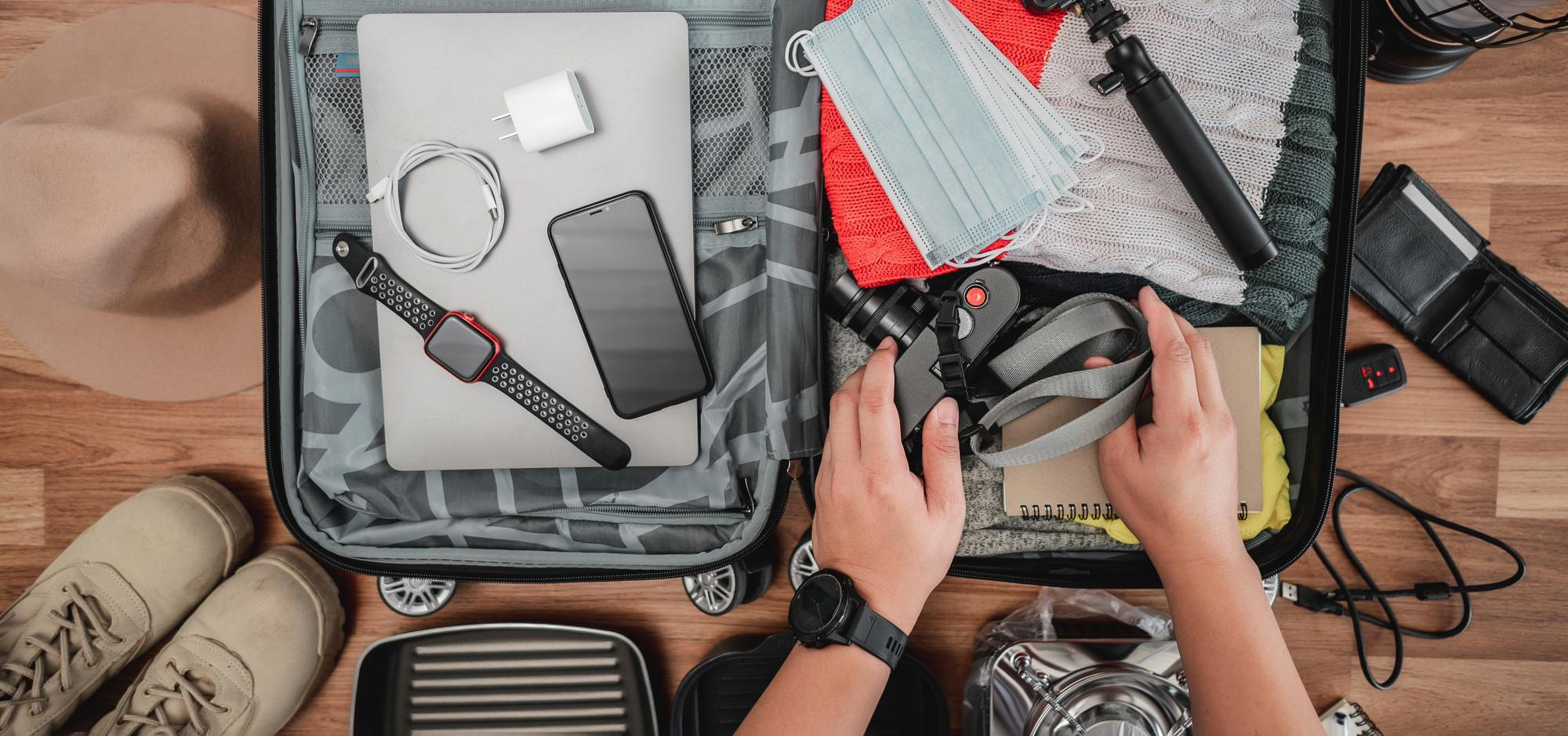 A person's hands rummage through an open suitcase filled with assorted travel items and clothing. 