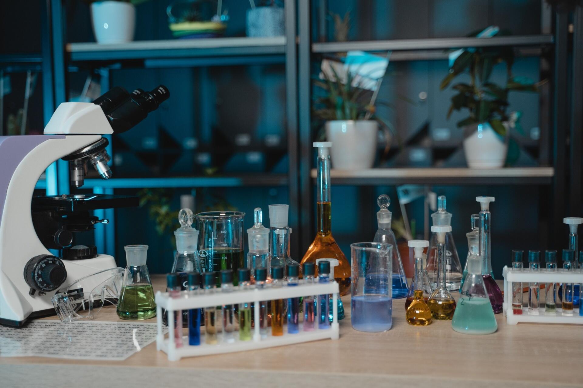 Chemistry laboratory equipment including test tubes, beakers, flasks, and a microscope arranged for practical experiments.
