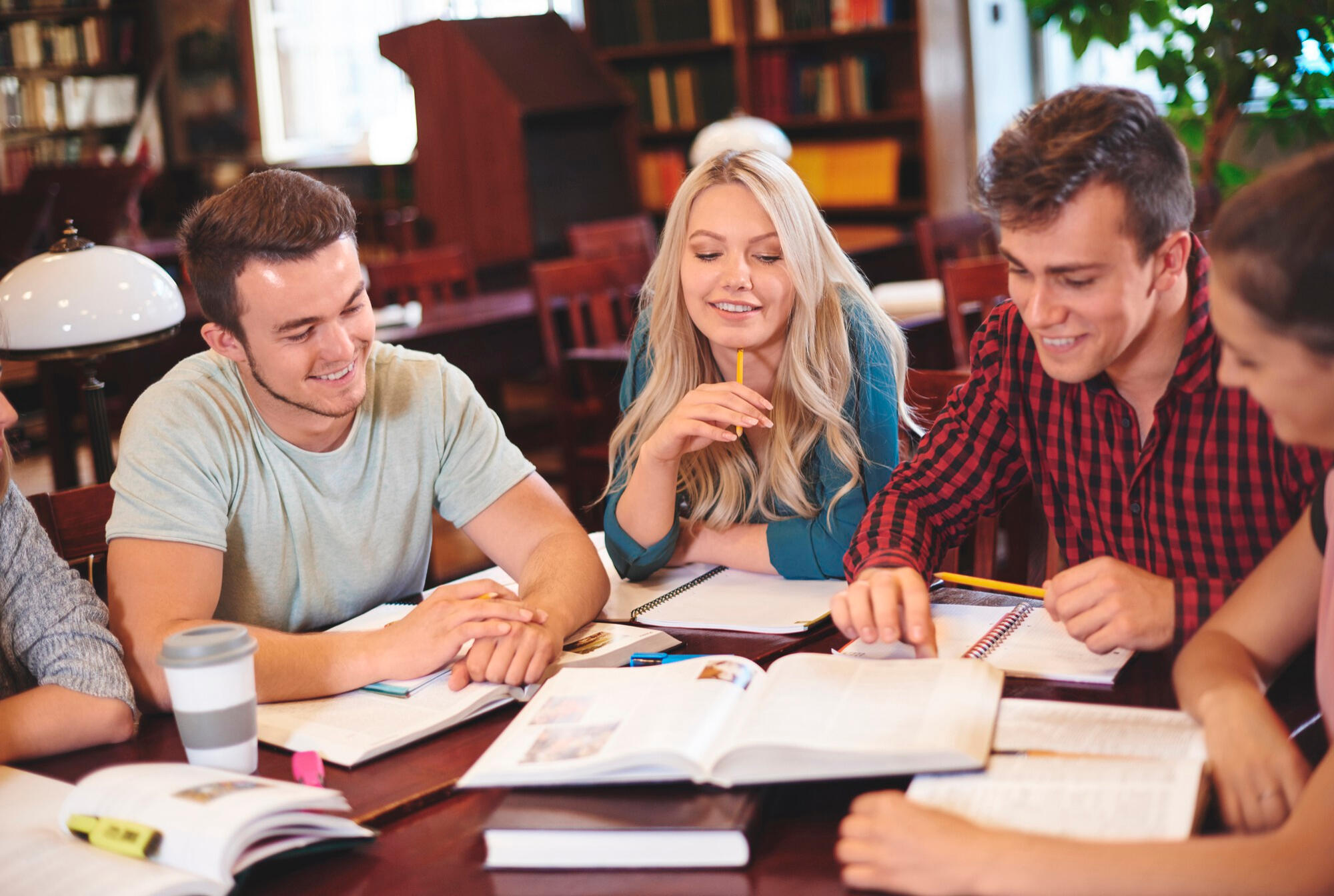 Group of young adults studying together with open books and notebooks in a cozy library setting.