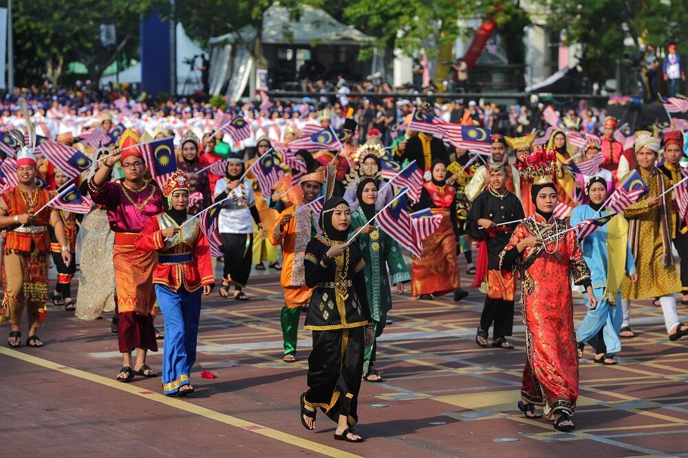 A vibrant cultural parade in Malaysia, participants in traditional attire proudly wave national flags, exuding a festive and patriotic atmosphere.