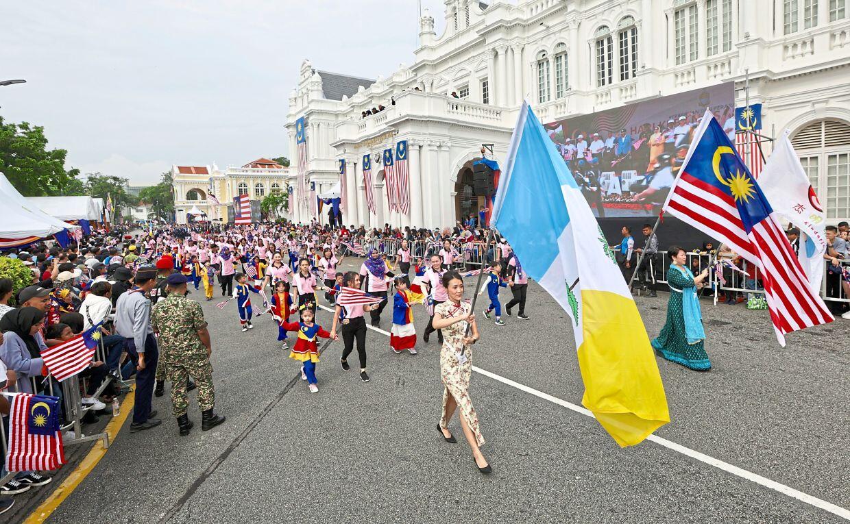Penang participants marching in a parade holding the Penang state flag and the national flag.