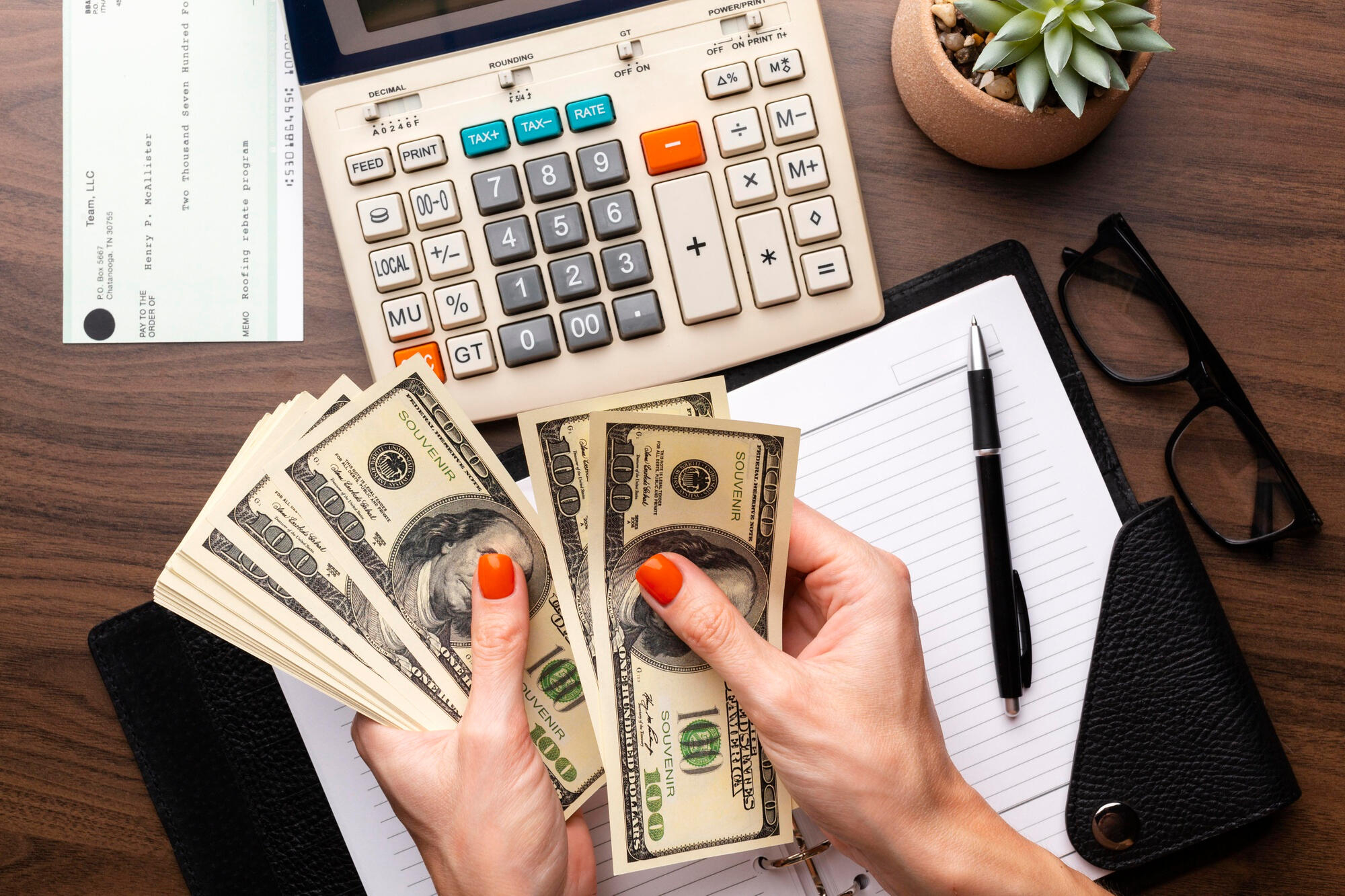 A woman's hands holding cash on a desk with a calculator and pen, indicating financial planning or budgeting.