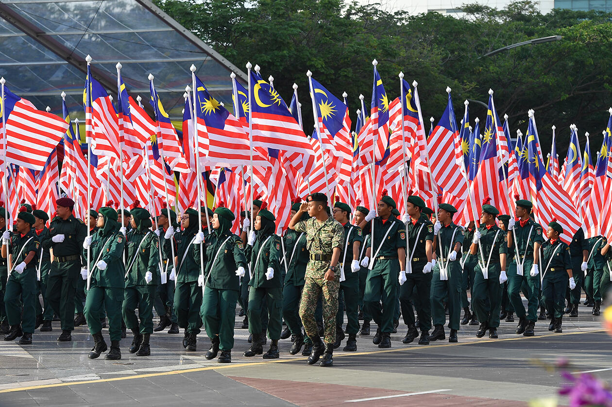 A group of uniformed officials marching holding the Jalur Gemilang.