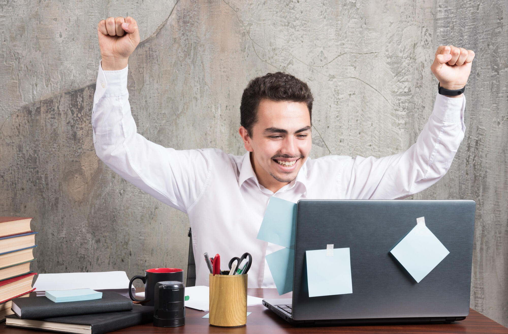 A man sitting at a desk with his arms raised, expressing excitement or celebration.