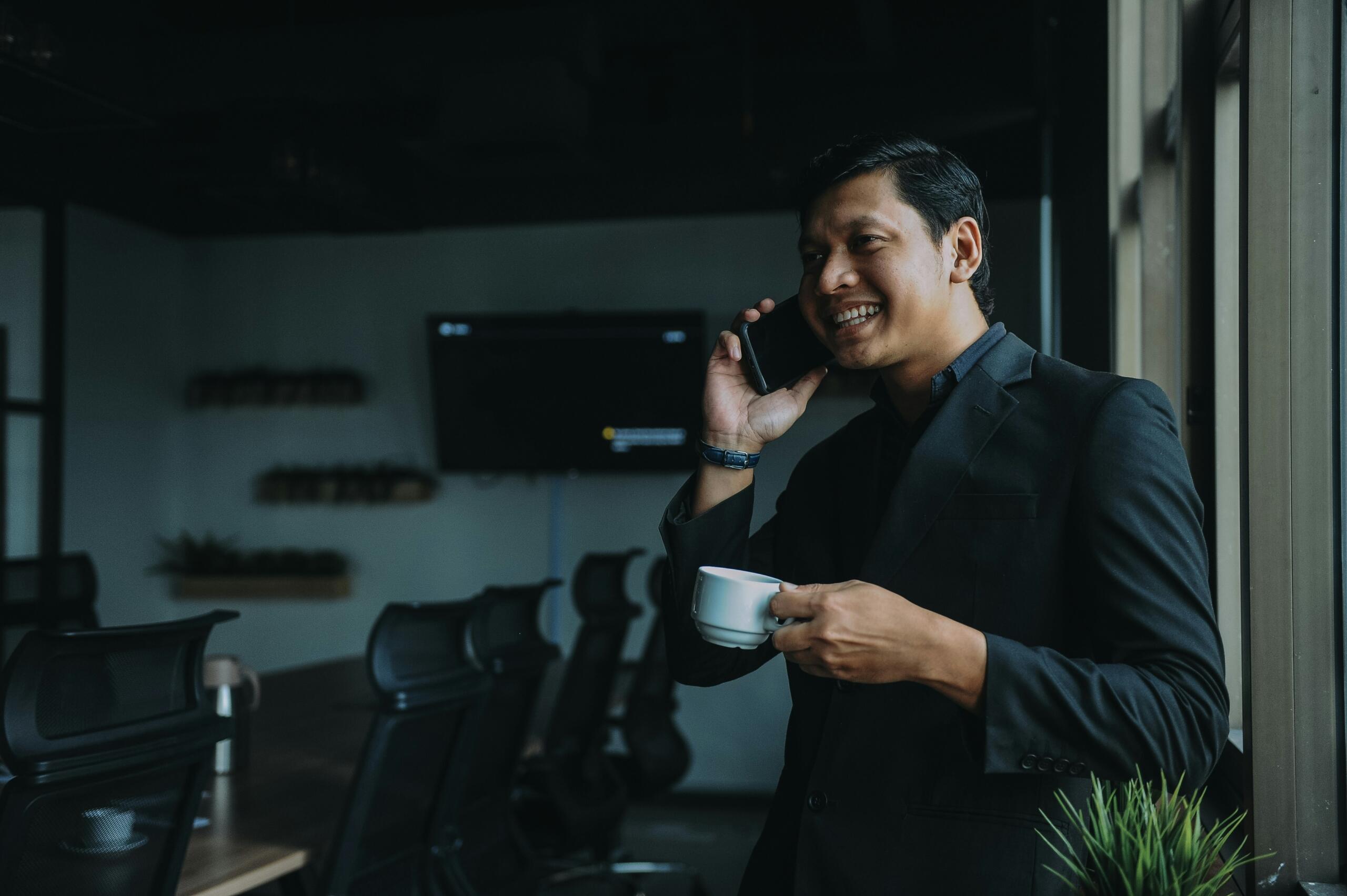Businessman engaged in a phone conversation, coffee cup in hand, in a professional environment.