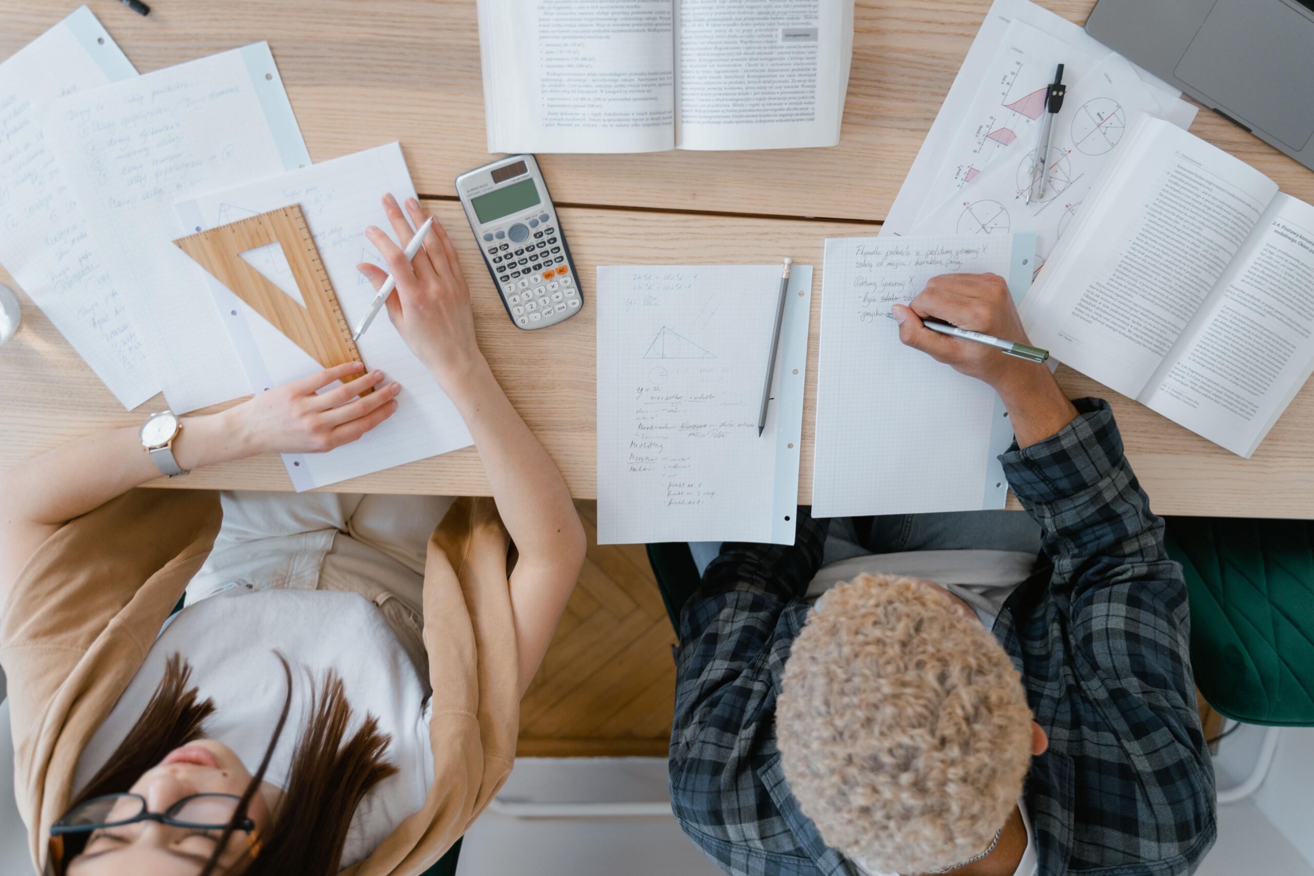 Students studying mathematics together with notes, calculators, rulers and geometry exercises on a desk.