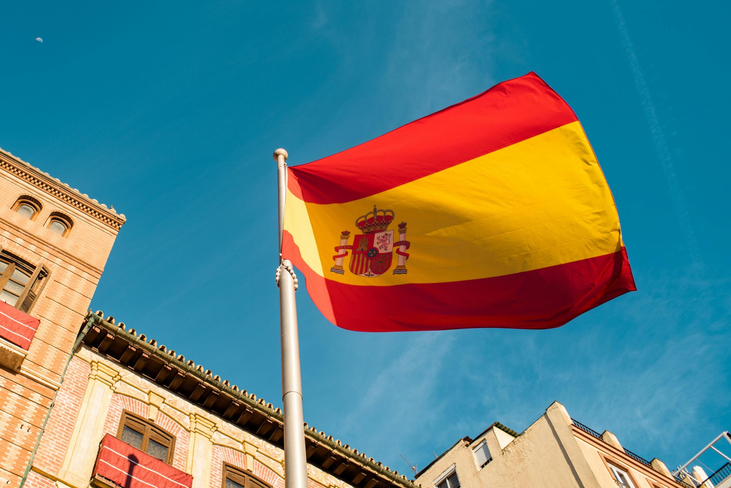 A Spanish flag waving in the wind against a clear blue sky.
