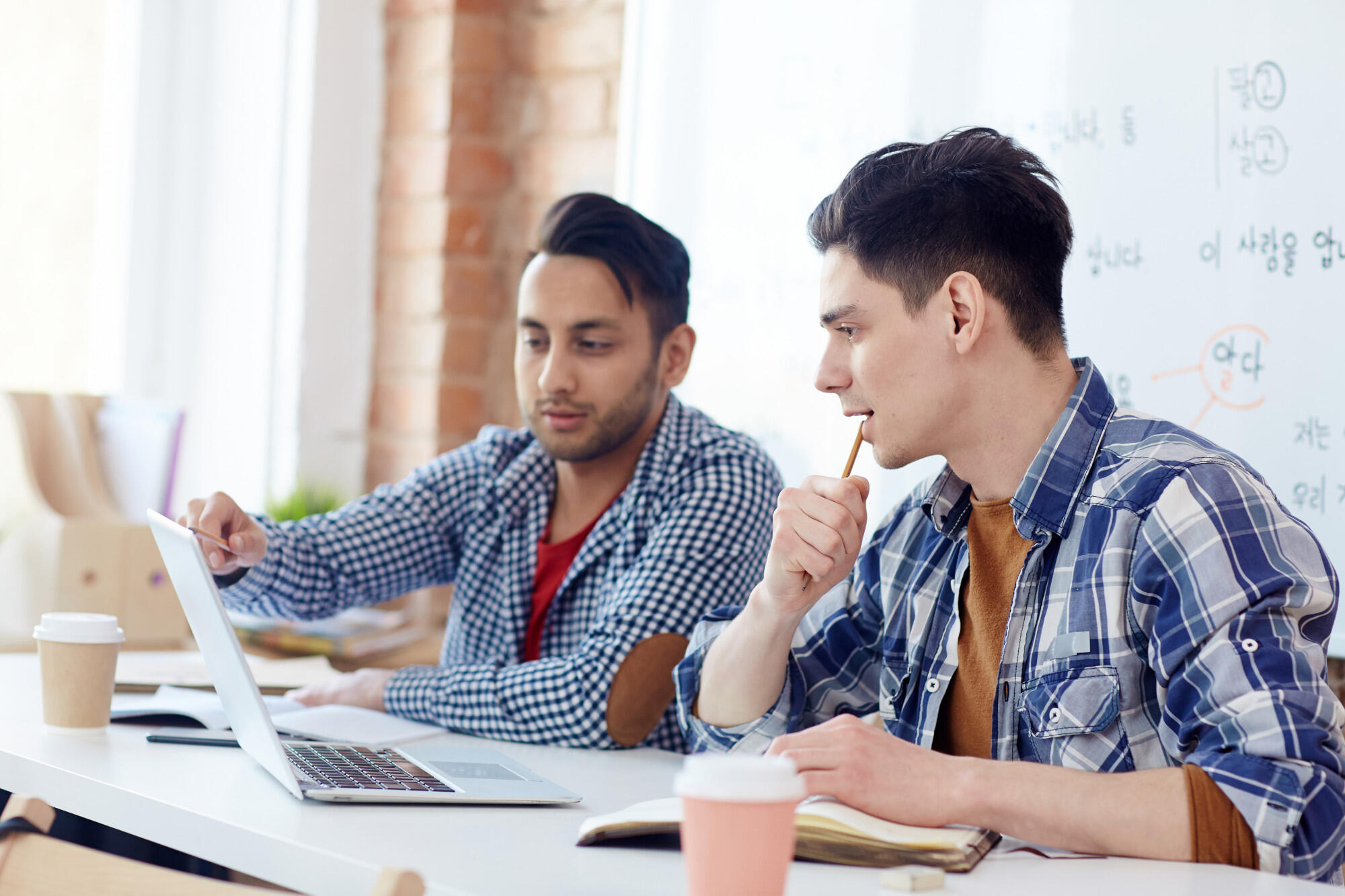 Two men seated at a table, each using a laptop, engaged in a discussion or collaborative work.