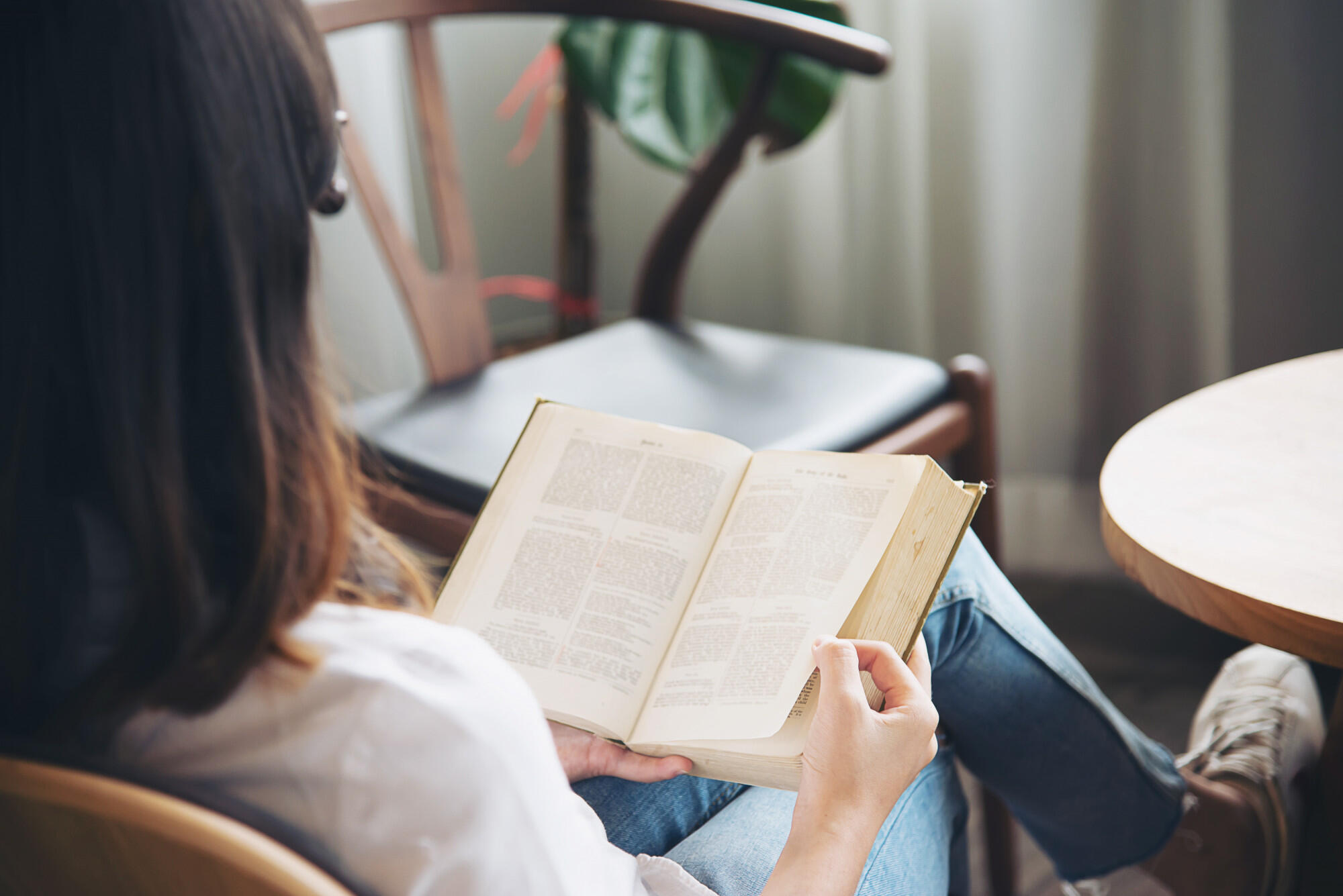 A woman comfortably sitting in a chair, focused on reading a book, surrounded by a cozy atmosphere.