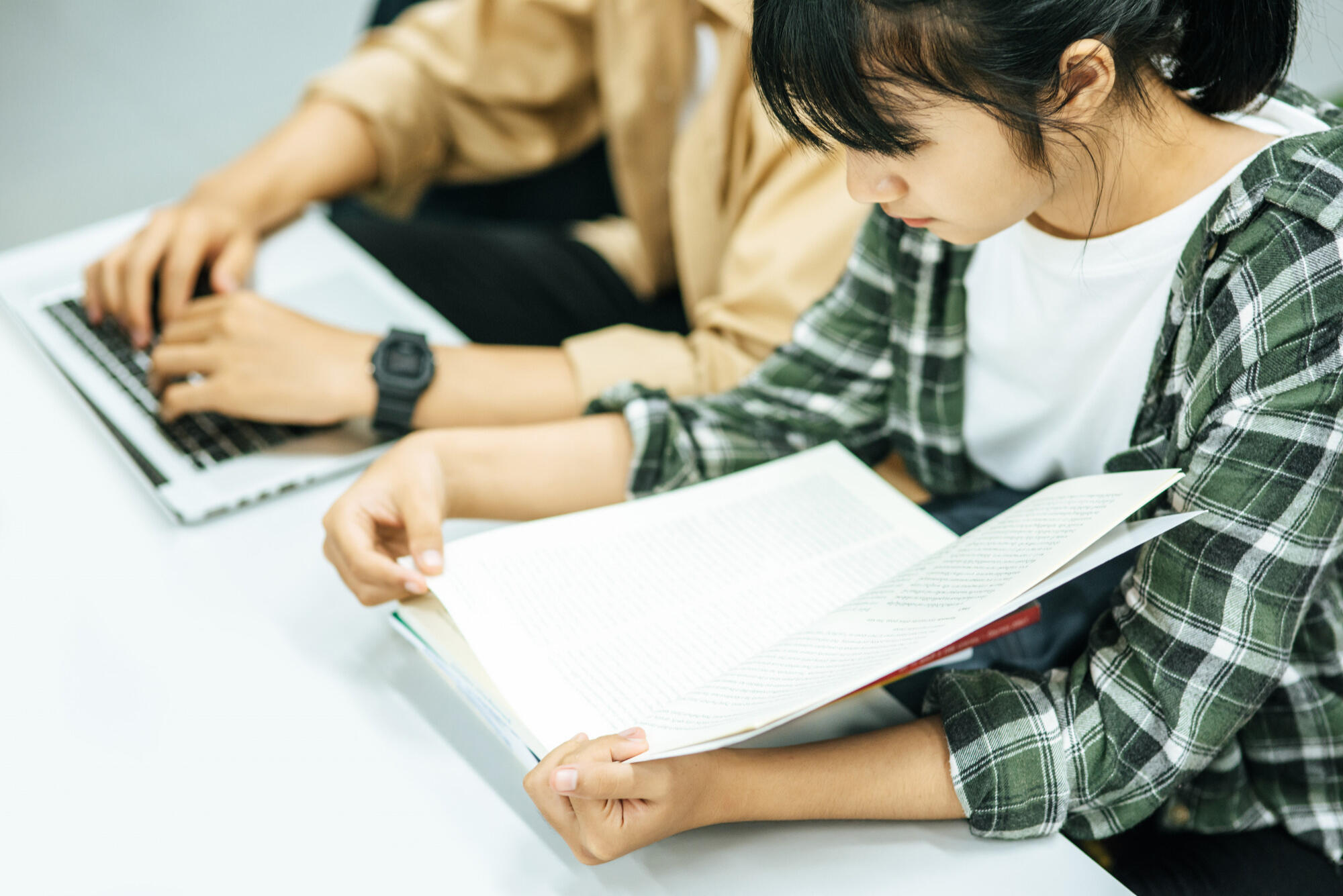 Asian student focused on studying at a library table, surrounded by books and notes.