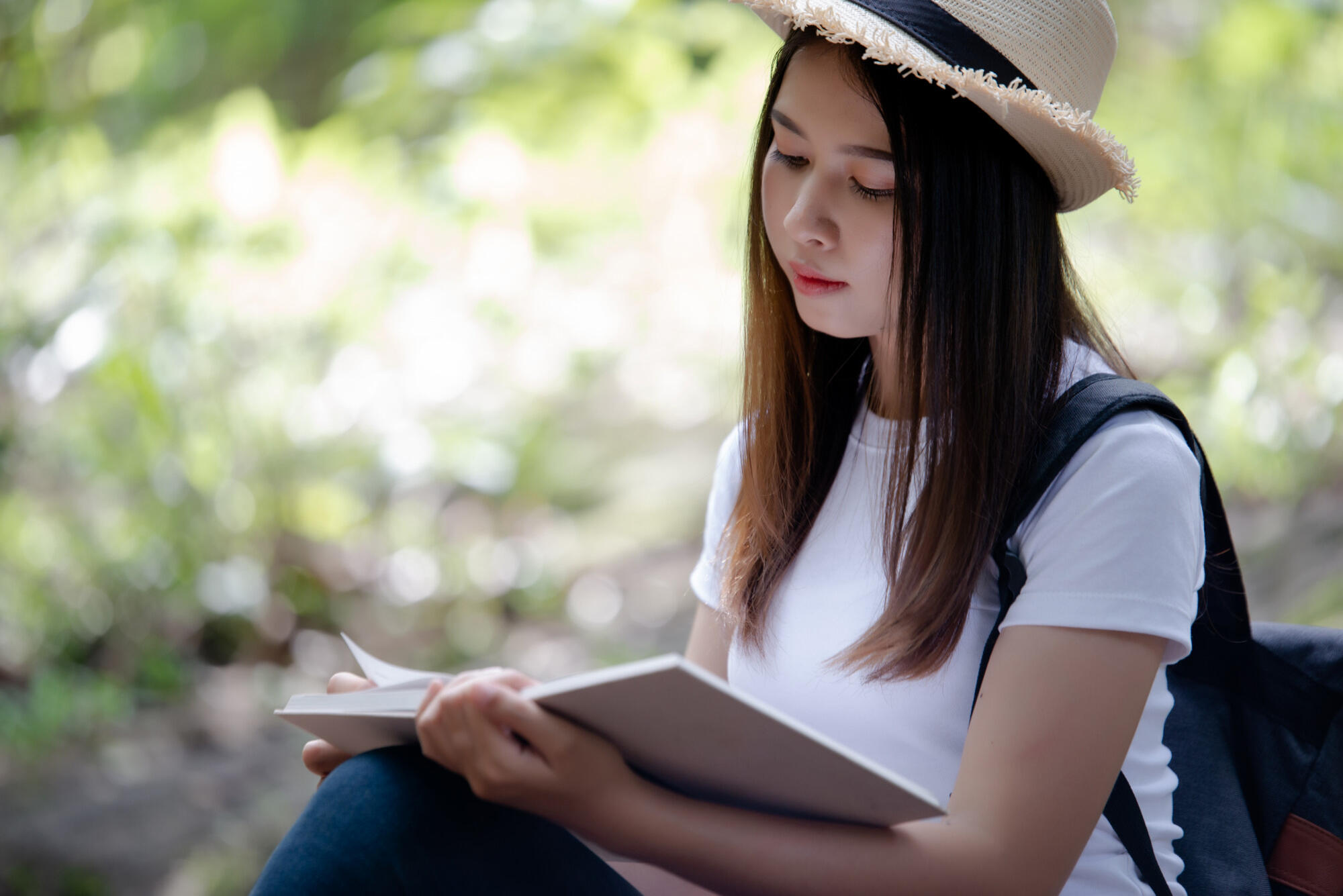 A woman with a hat is deeply engaged in reading a book, showcasing a moment of tranquility.