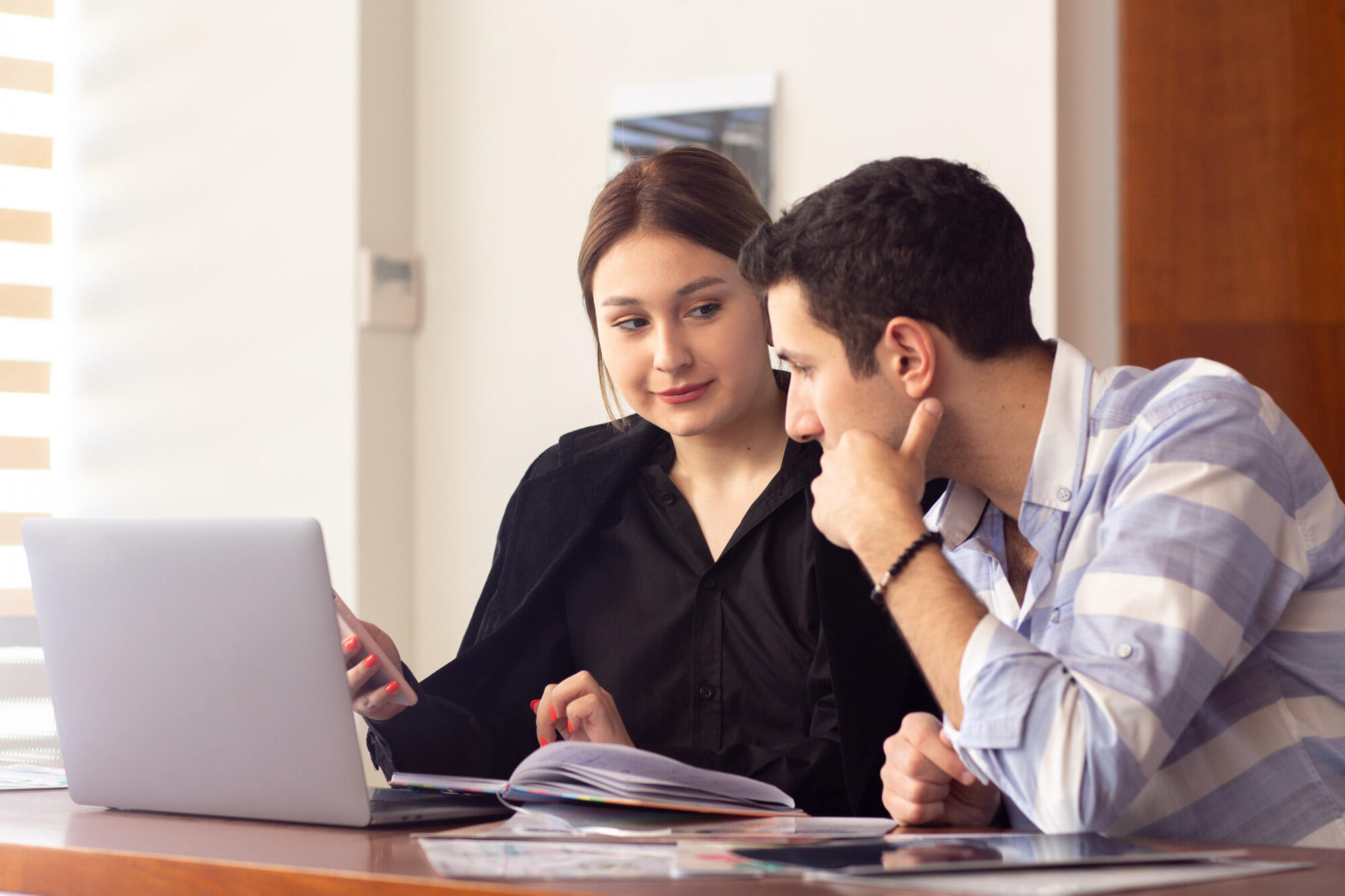 A man and woman collaborate at a table, both engaged with a laptop in front of them.