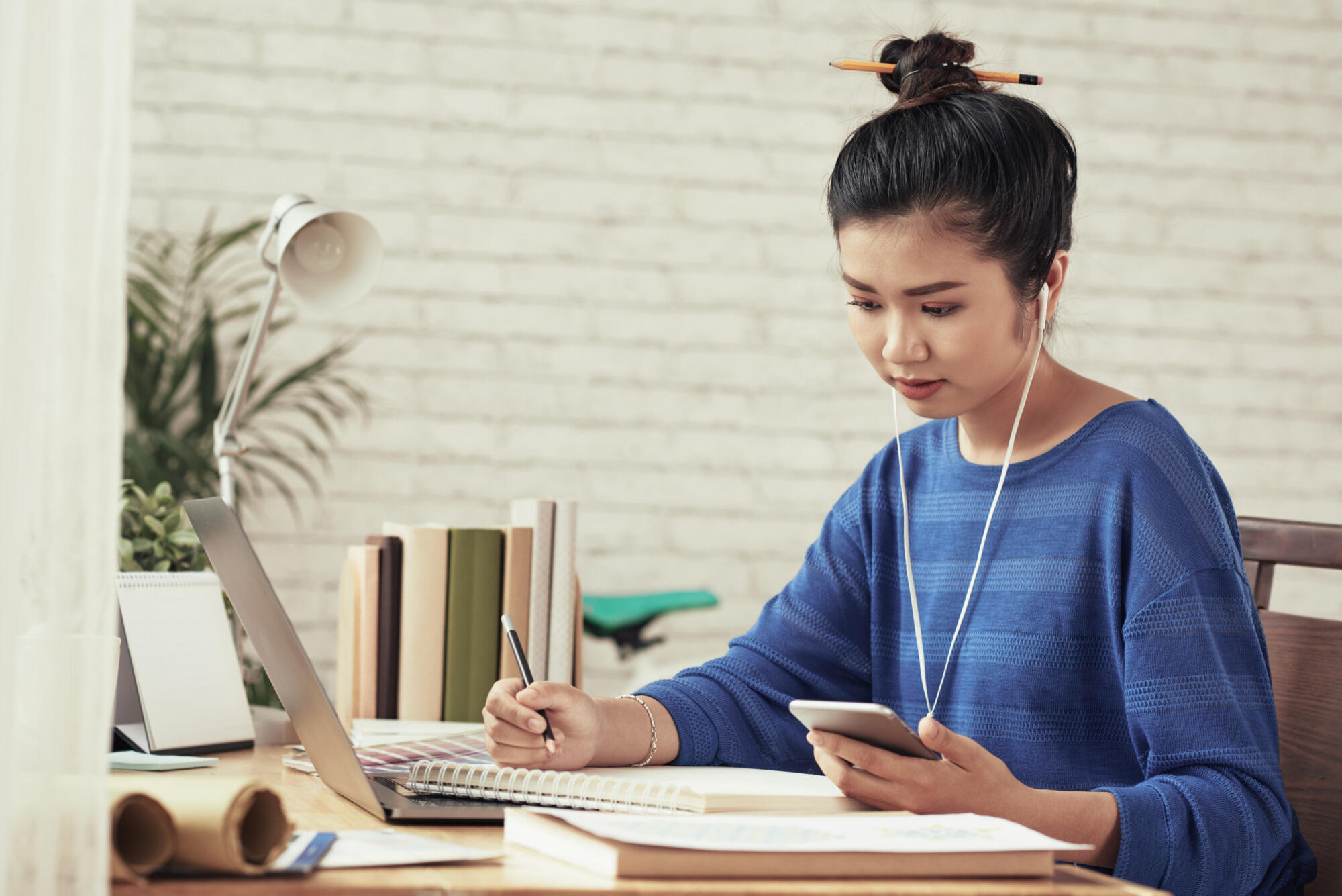 A woman seated at a desk, working on a laptop with a cell phone beside her.