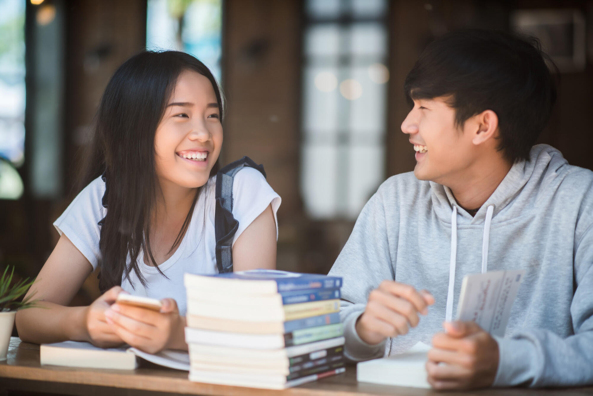 Asian couple studying together at a library table, surrounded by books and laptops, focused on their work.
