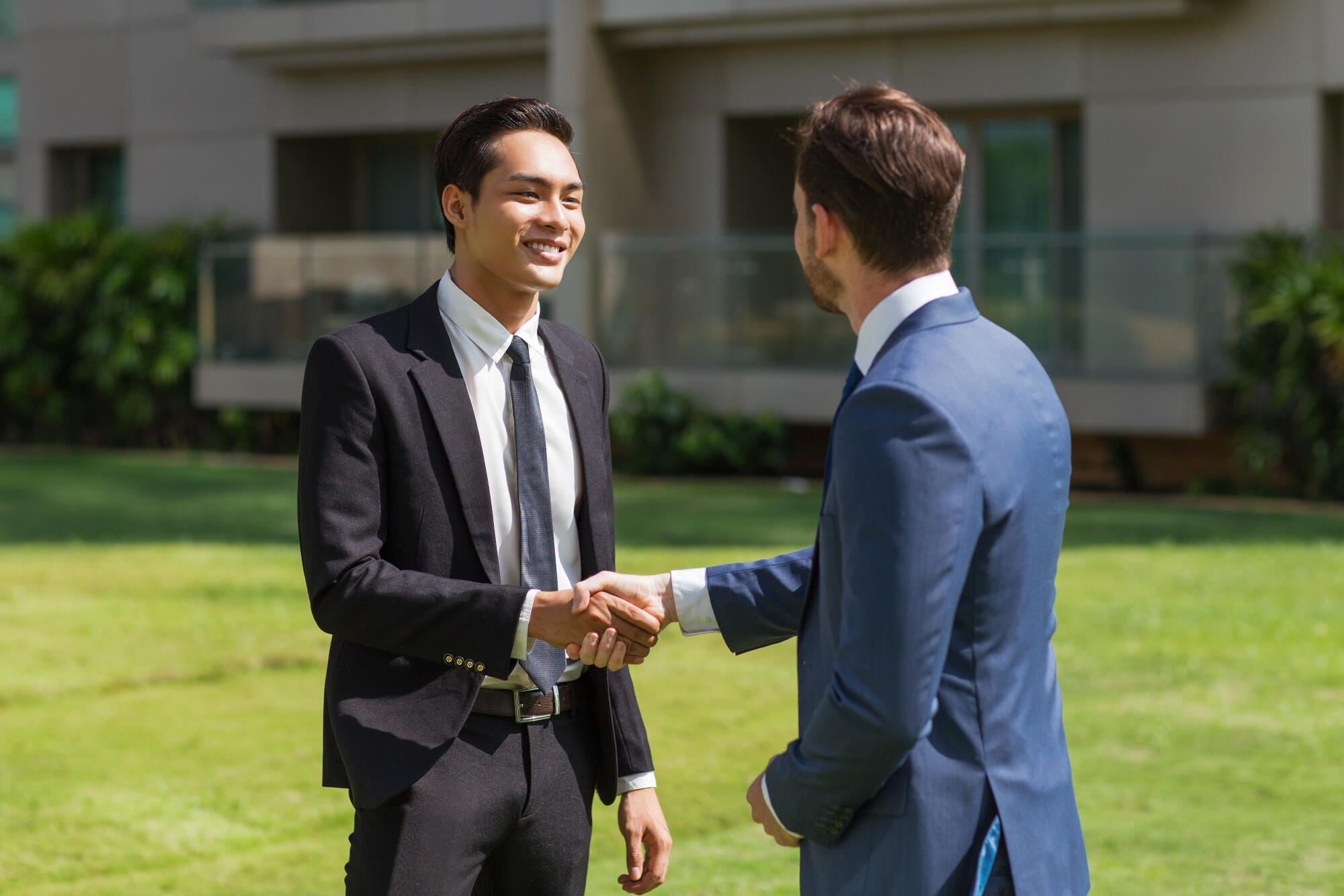 Two men shaking hands in front of a modern building, symbolizing a business agreement or partnership.