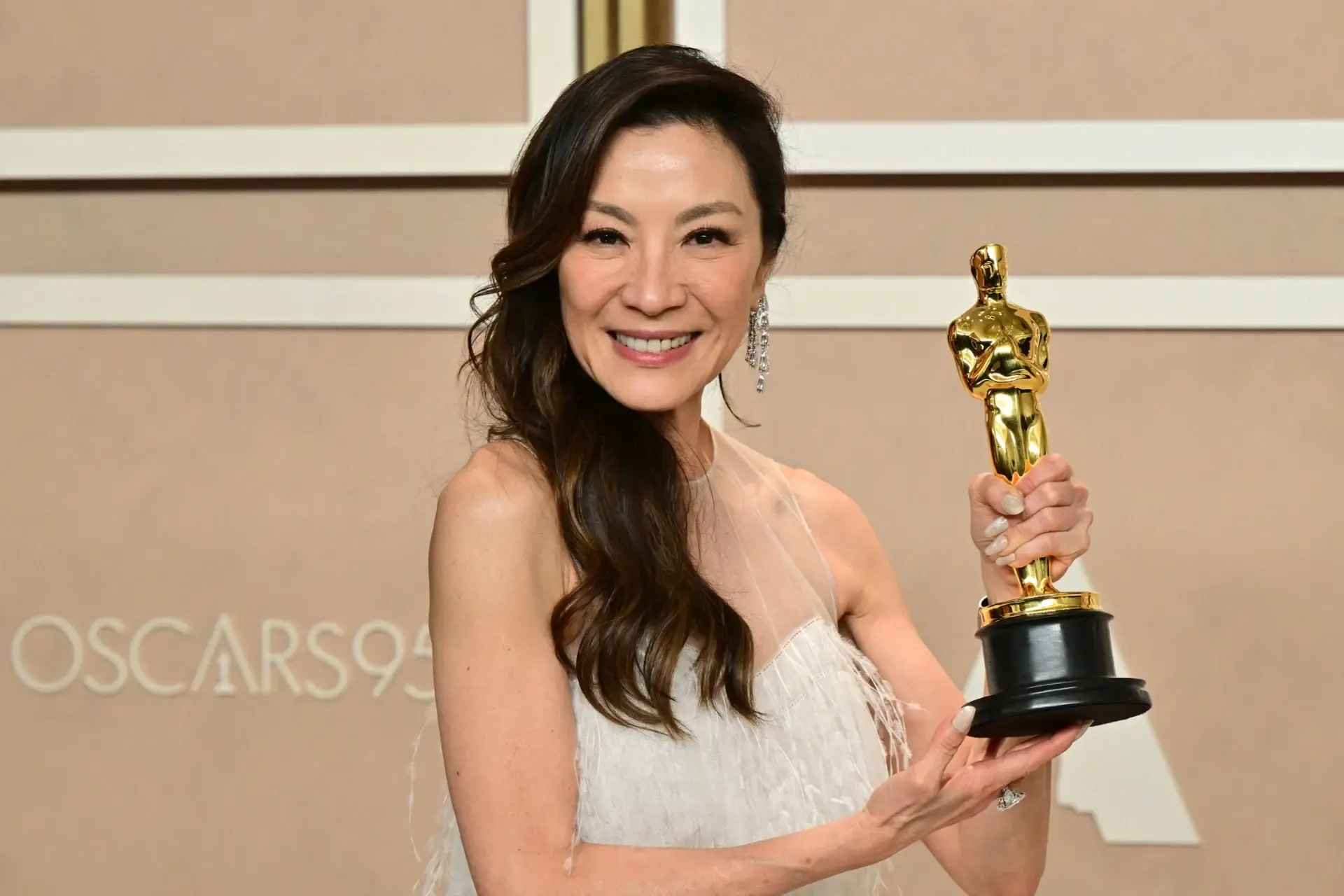 Malaysian actress Michelle Yeoh smiling and holding her Best Actress Oscar for Everything Everywhere All at Once at the 95th Academy Awards in 2023.