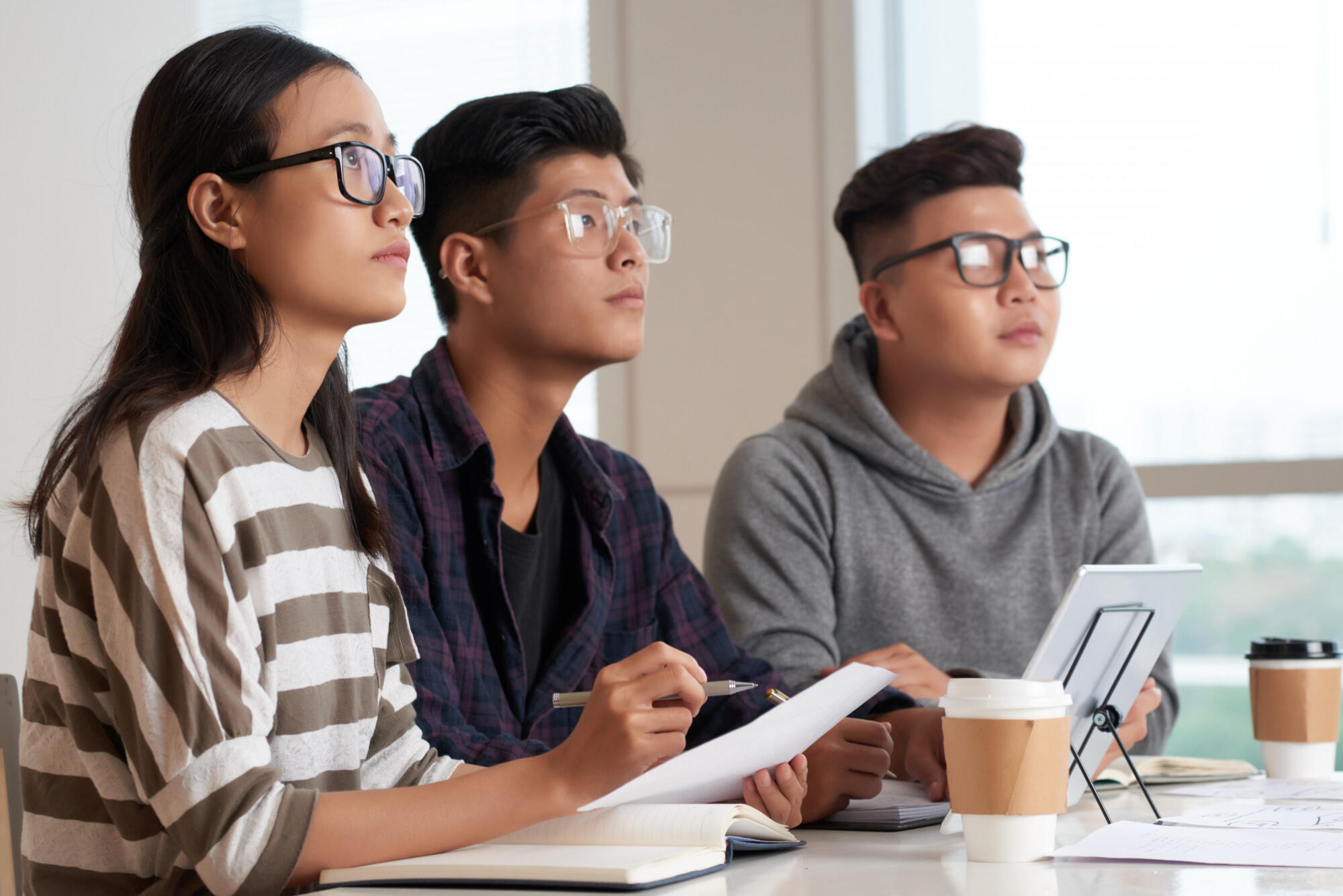 A group of three young people around a table, focused on a laptop, discussing ideas together.