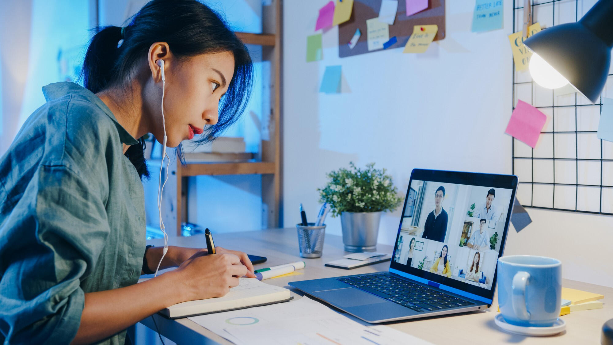 A woman focused on her laptop, seated at a desk with a notepad and pen beside her.