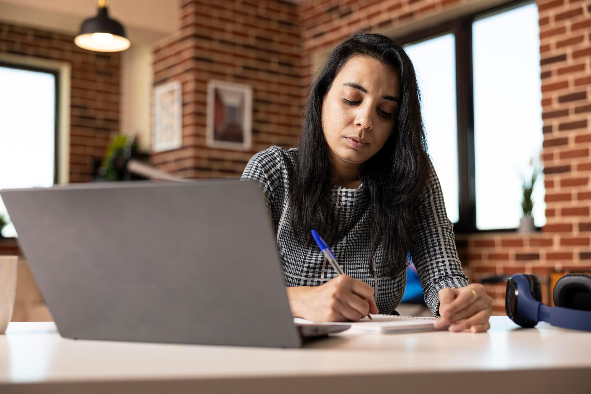 A woman at a desk, using a laptop while holding a pen, engaged in her work.