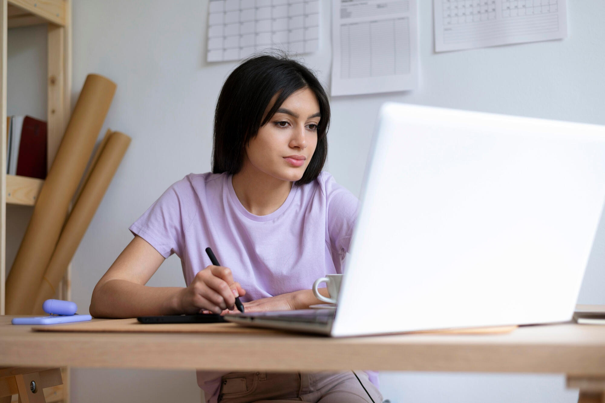 A woman at a desk using a laptop, with a coffee mug and documents arranged around her workspace.