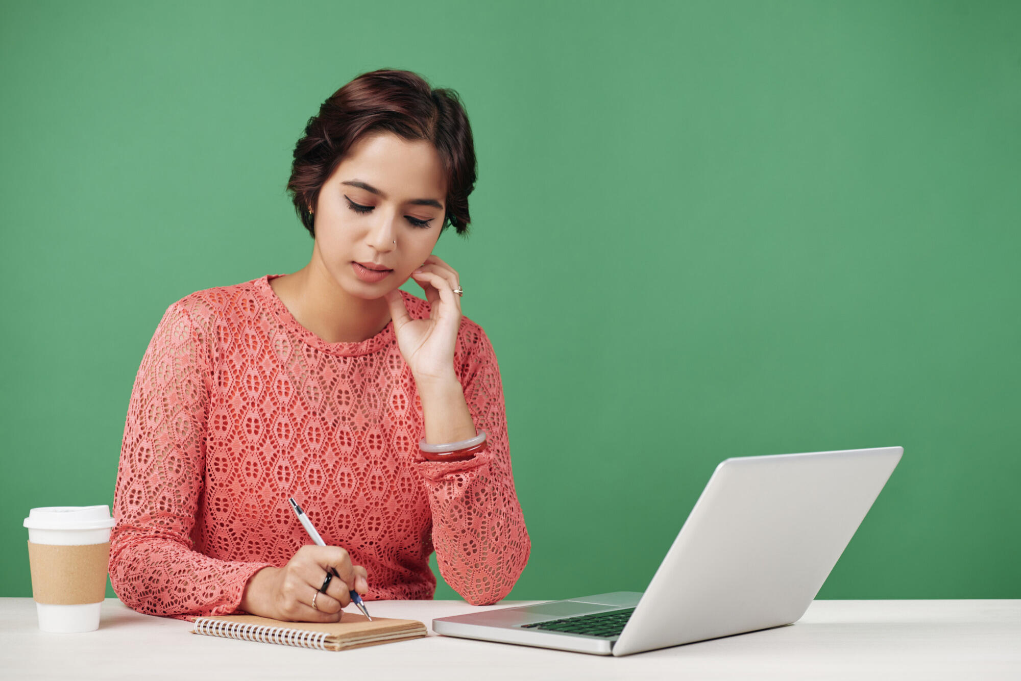 A woman seated at a desk, working on a laptop with a cup of coffee beside her.