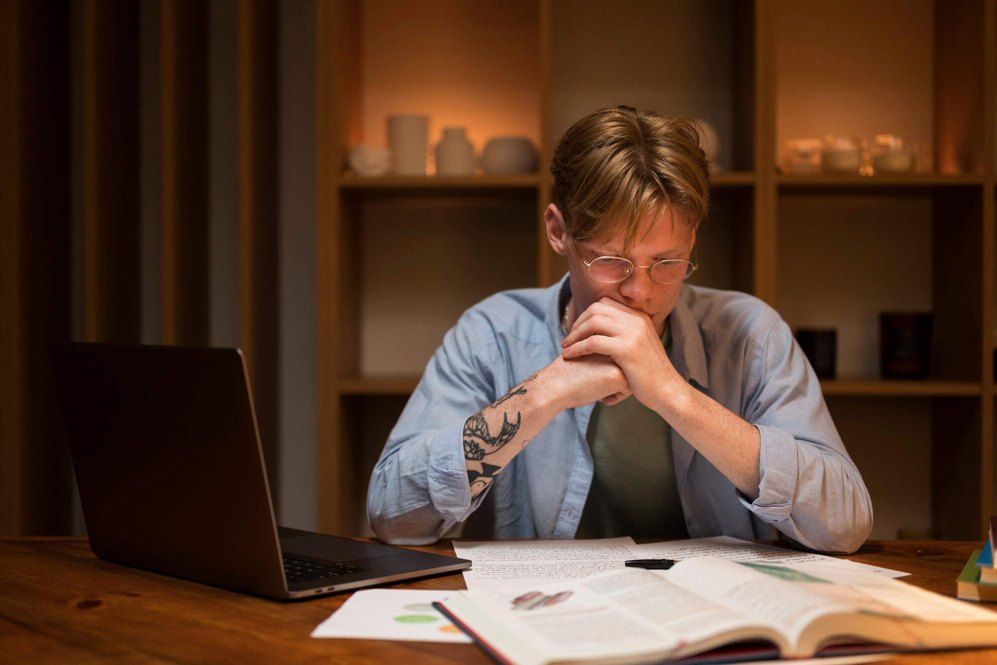 A man at a table using a laptop, with books and papers spread out around him for study.