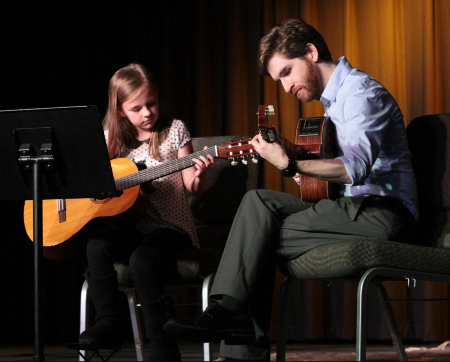 A guitar teacher teaching a child