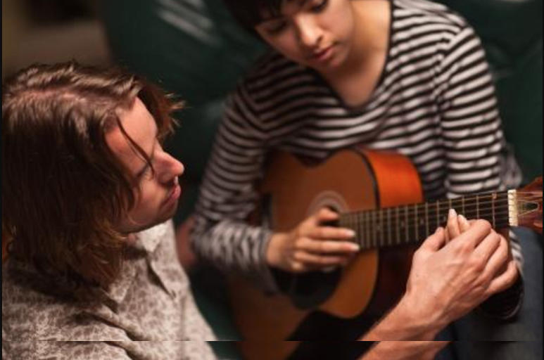 A teacher helps a child learn guitar chords.