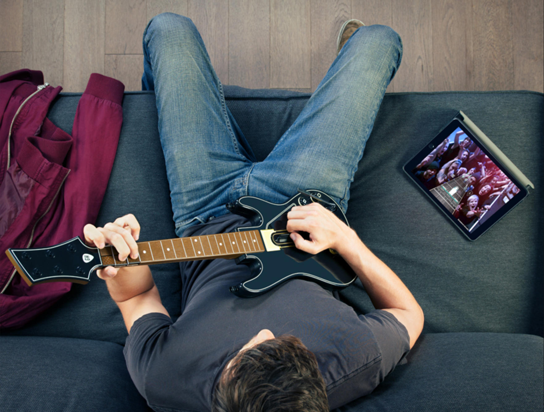 A man playing guitar hero on the couch (learn guitar instead)