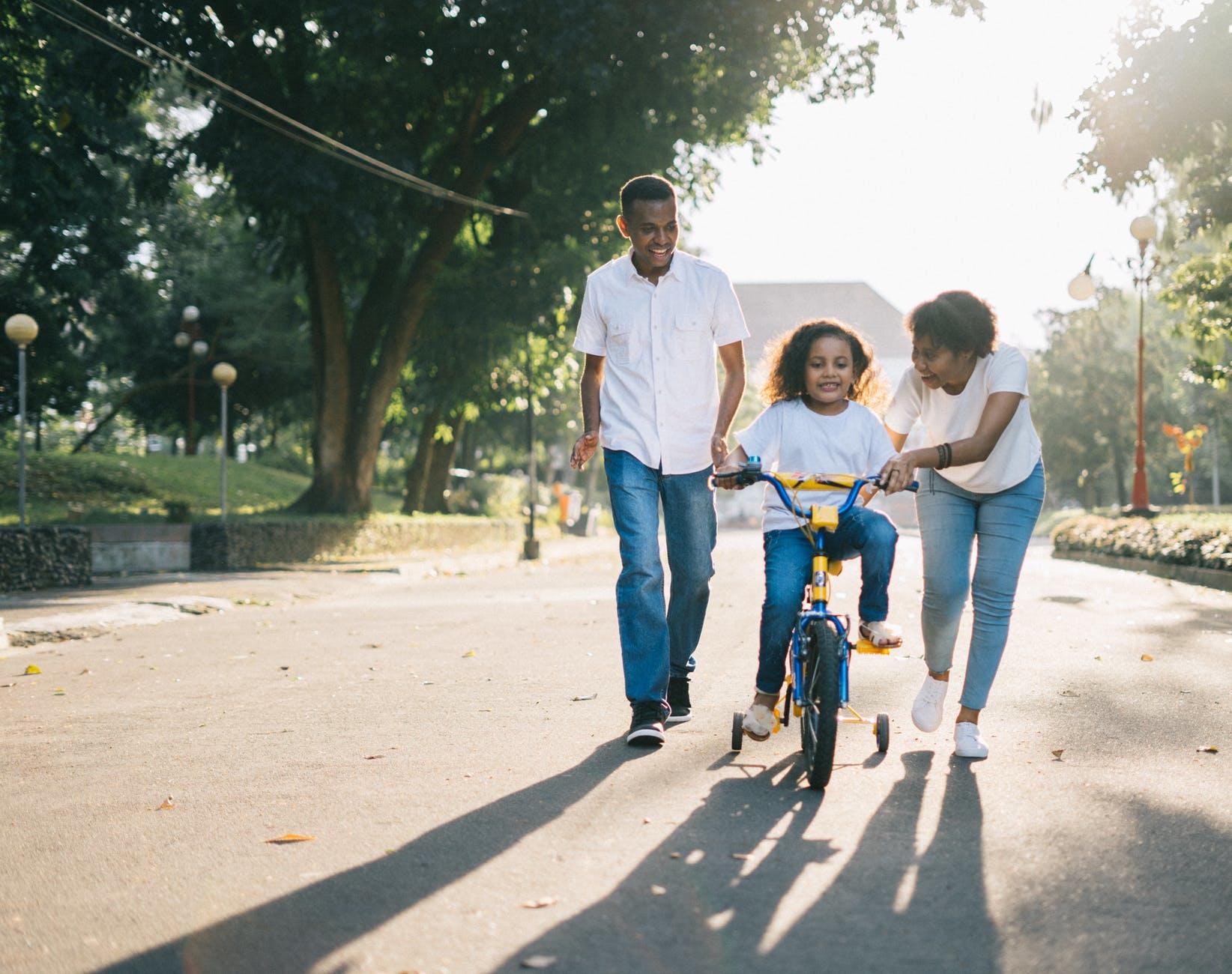 Twee volwassenen helpen kind op fiets