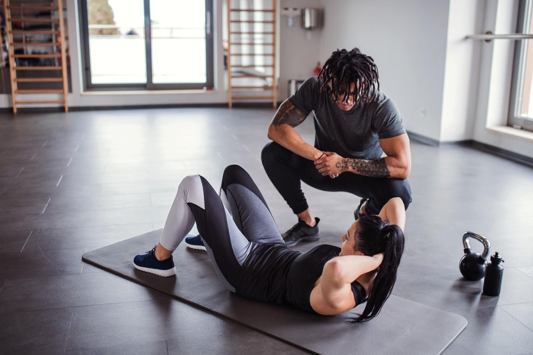 vrouw oefent in gymzaal onder begeleiding van trainer