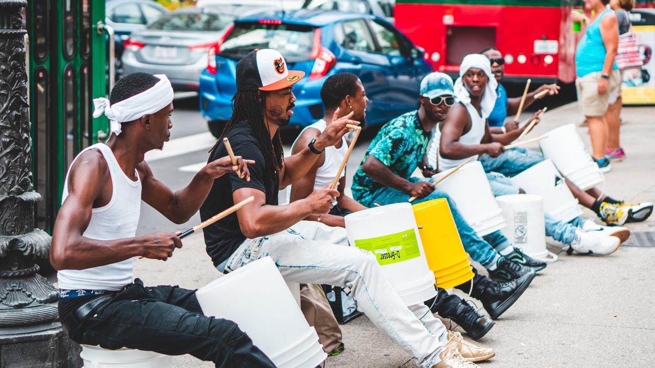 Een aantal mannen zittend op straat drummend op plastic emmers