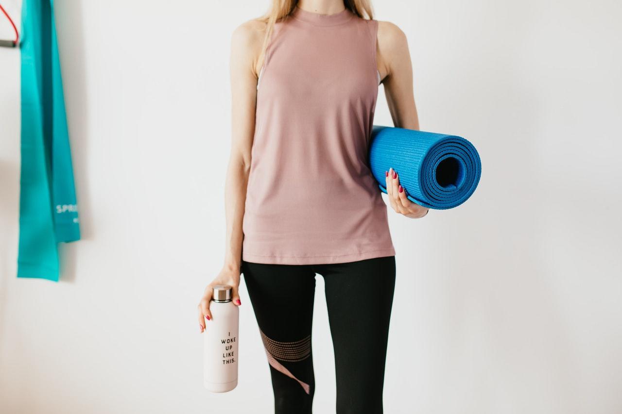 Persoon met met yoga mat onder de arm en flesje