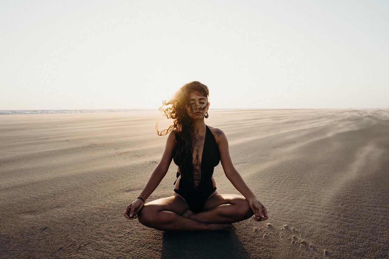 Een vrouw zit in de zon en doet yoga.
