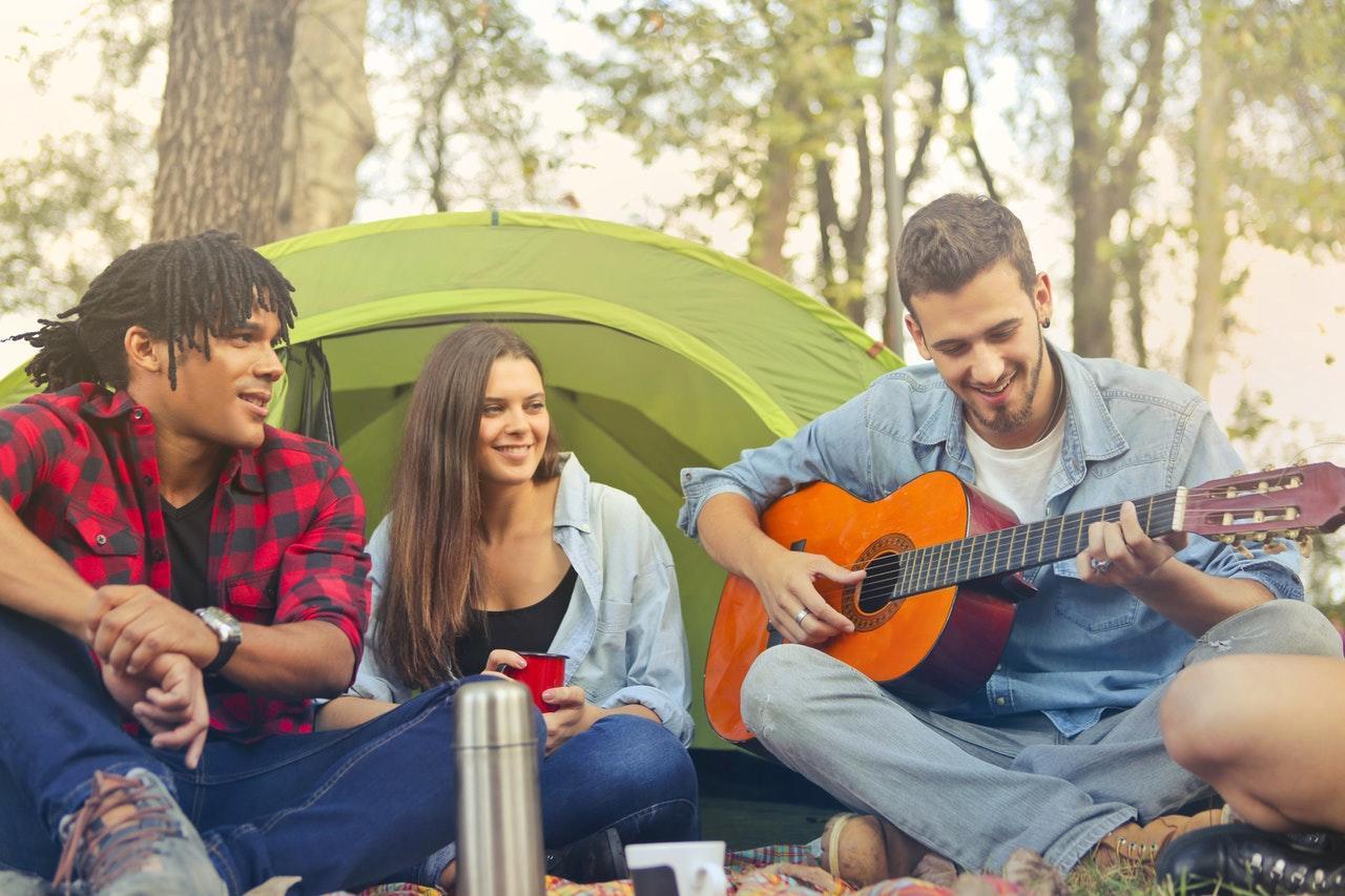 Persoon die gitaar speelt voor twee mensen voor tent